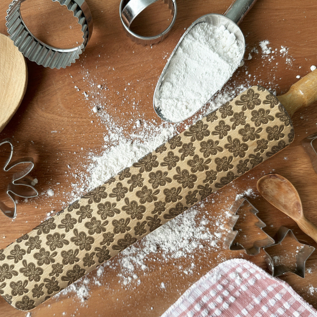 Rolling pin with floral patterns on a wooden surface with flour and cookie cutters.
