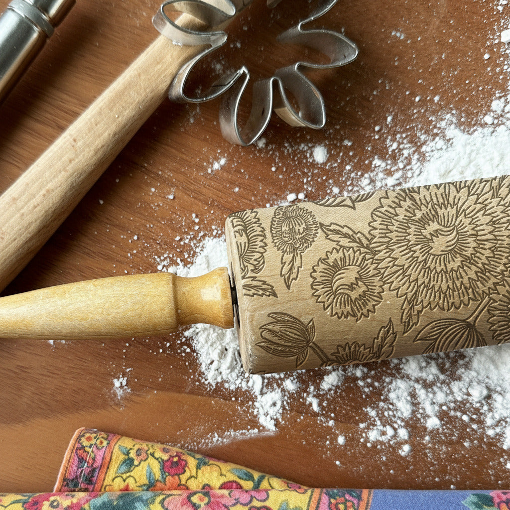 Decorative rolling pin with floral patterns on a wooden surface with flour, next to a cookie cutter.