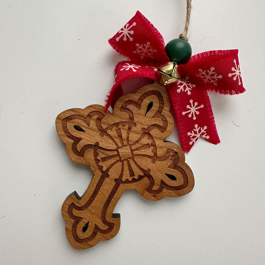 Wooden cross ornament with a red ribbon and green bead on a white background