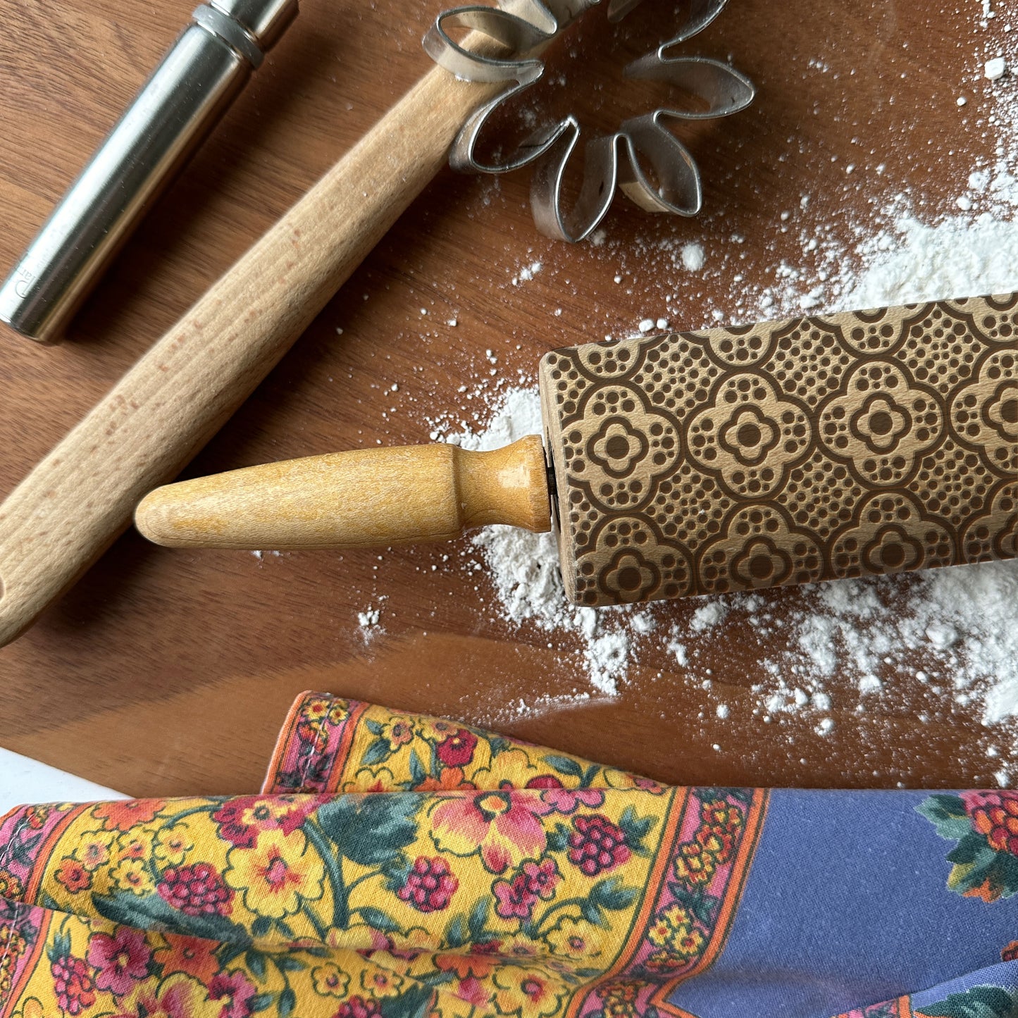 Decorative rolling pin with intricate patterns on a wooden surface with flour and a floral towel.