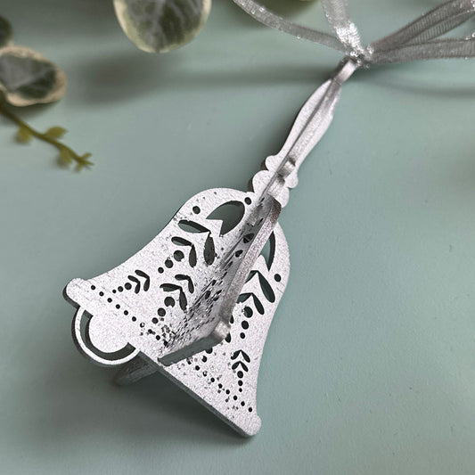 Silver bell-shaped pendant on a light blue background with green leaves.
