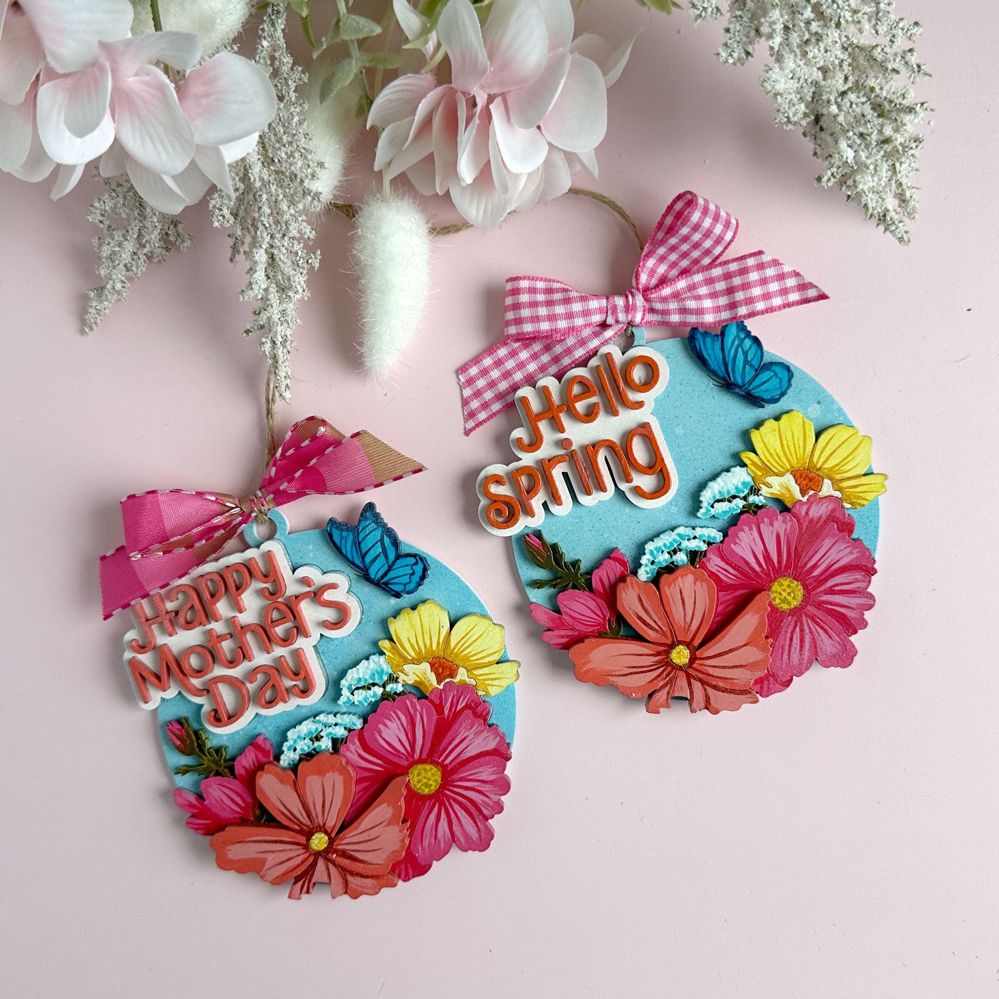 Two decorative ornaments with floral designs and text on a pink background