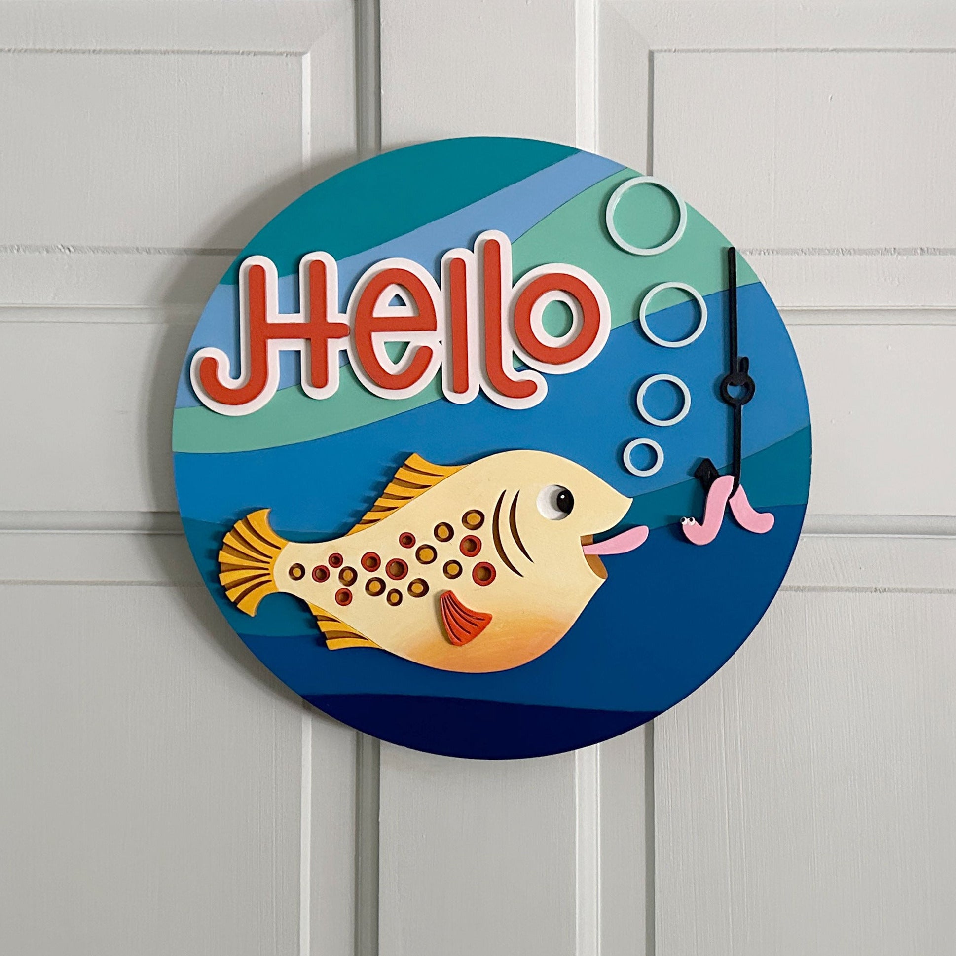 Round decorative sign with a fish and 'Hello' text on a white door.