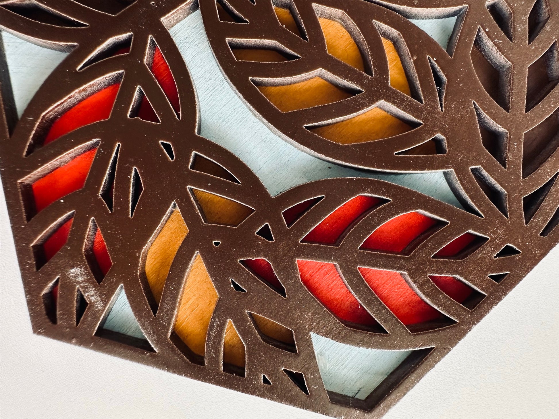 Decorative coaster with cut-out leaf patterns and colored background on a white background