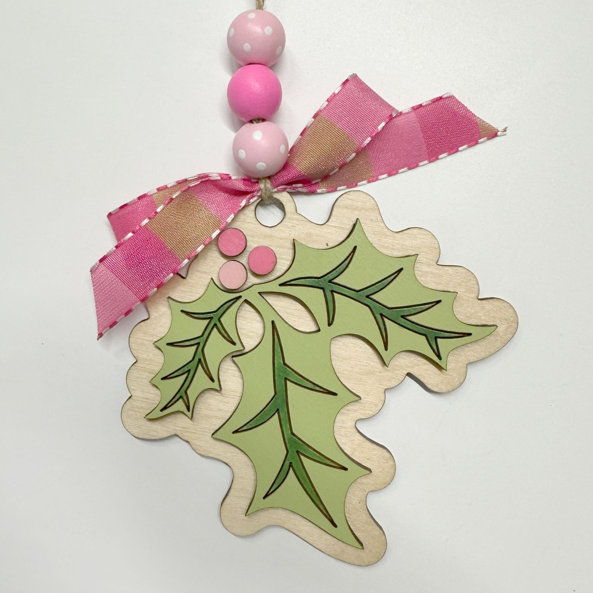 Decorative holly leaf tag with pink ribbon and beads on a white background