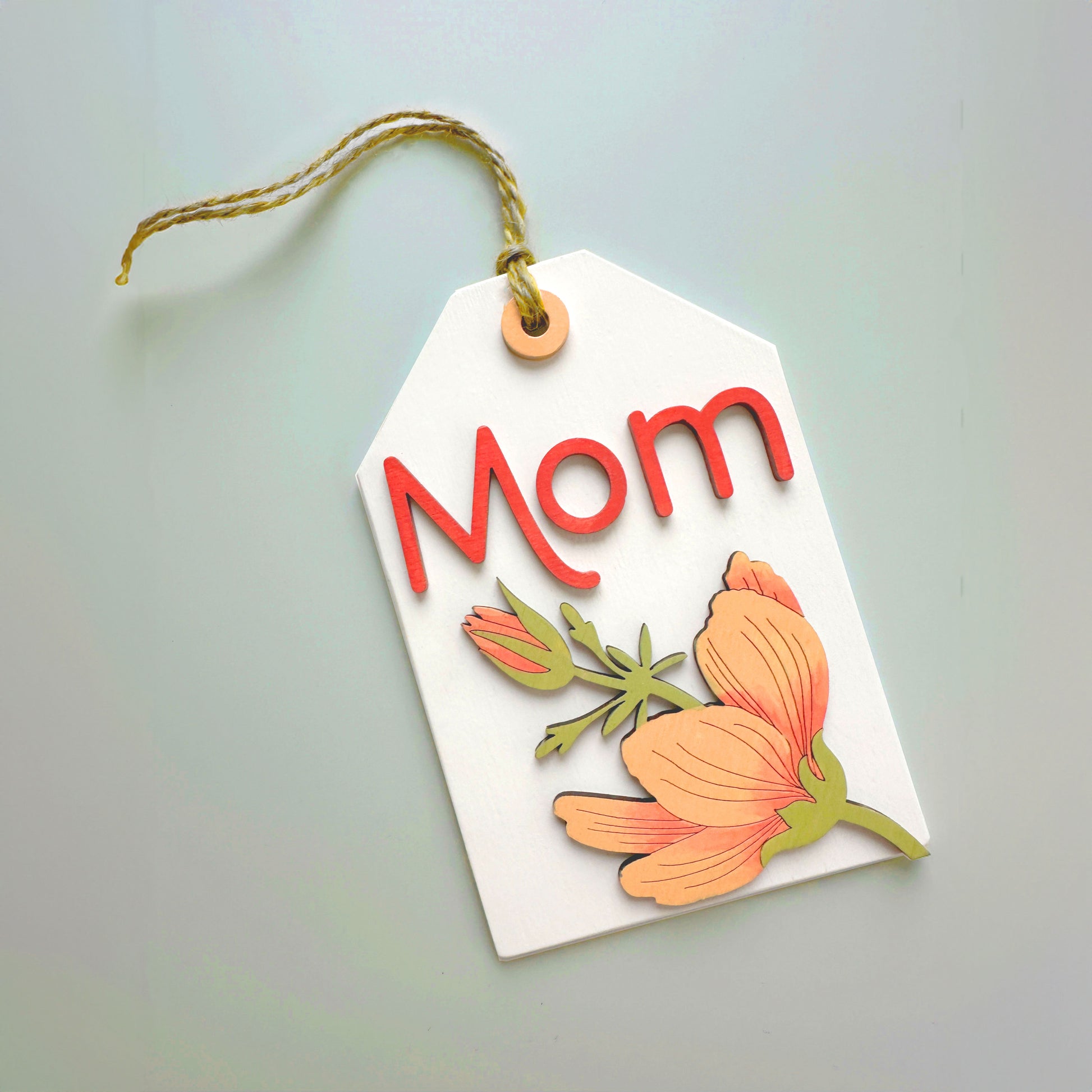 Decorative tag with 'Mom' and floral designs on a light gray background