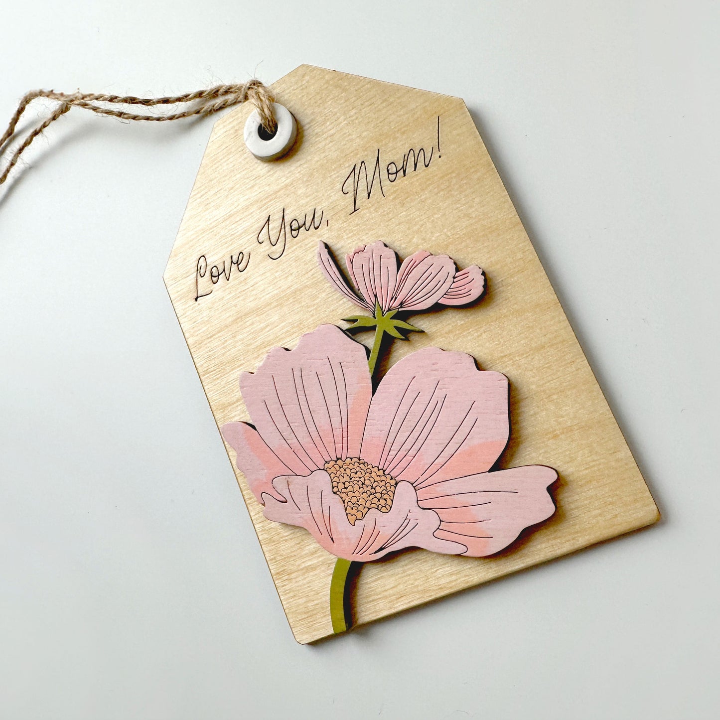 Kraft paper tag with pink floral cutout and string on a light gray background