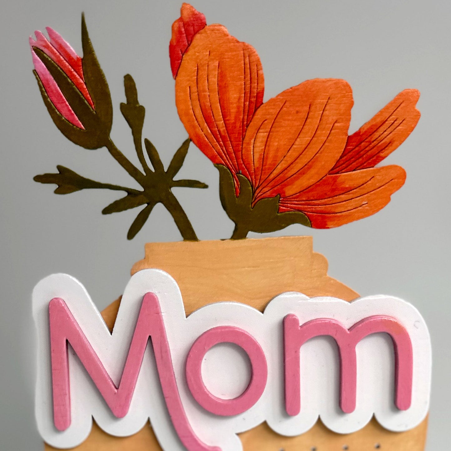 Decorative earring stand with flowers and 'Mom' text on a gray background