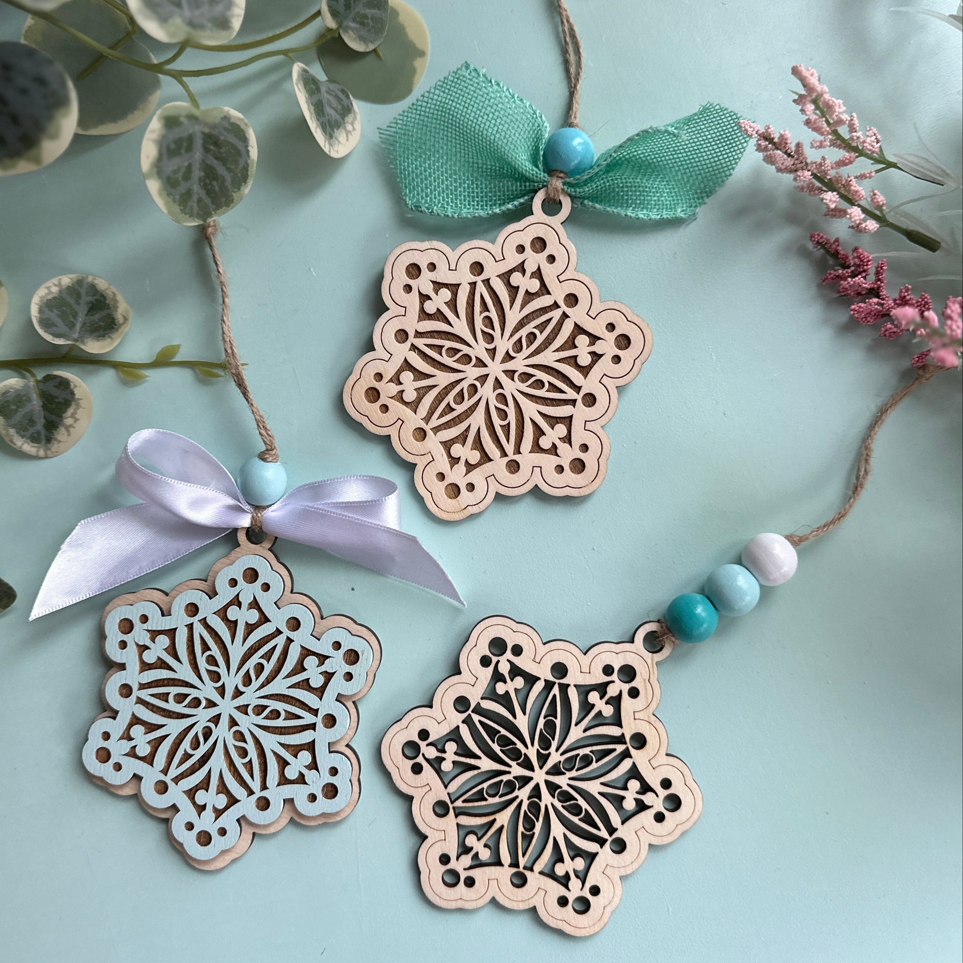 Decorative wooden snowflake ornaments with ribbons and beads on a light blue background