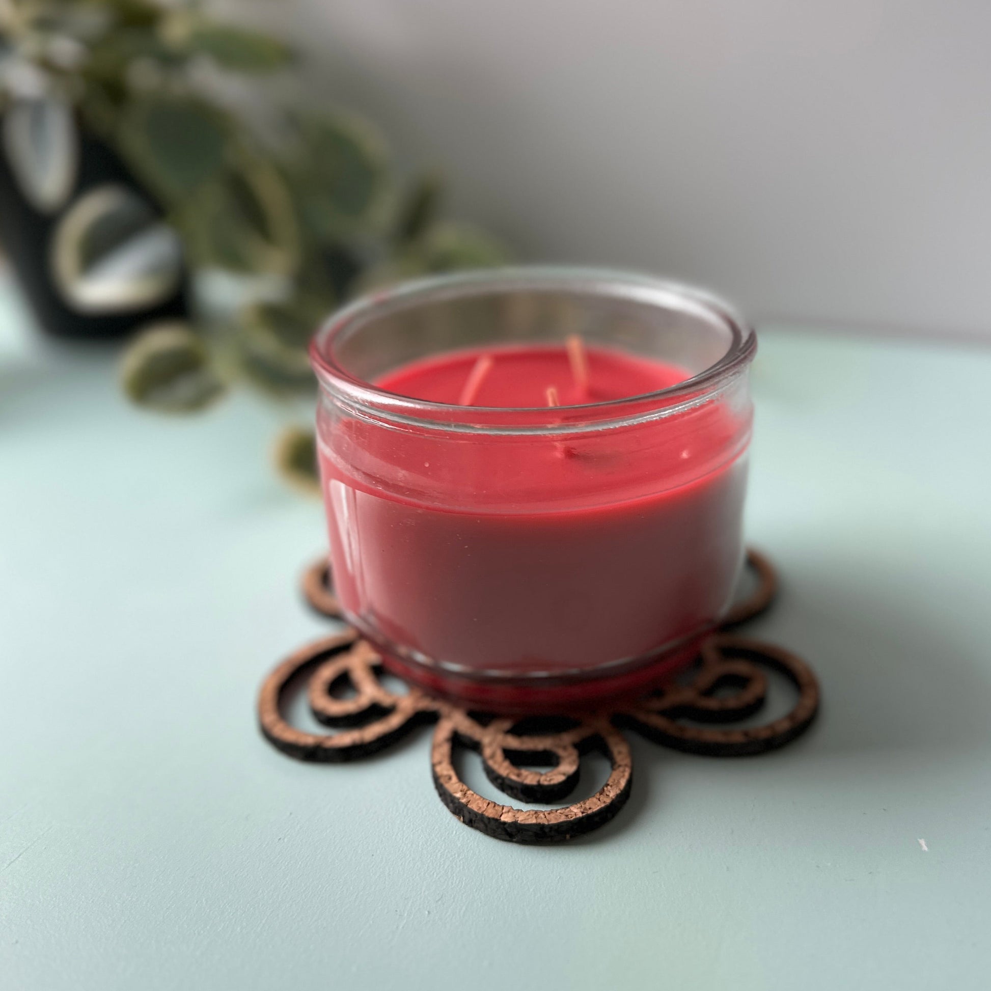 Pink candle in a glass jar on a decorative coaster with a blurred plant in the background