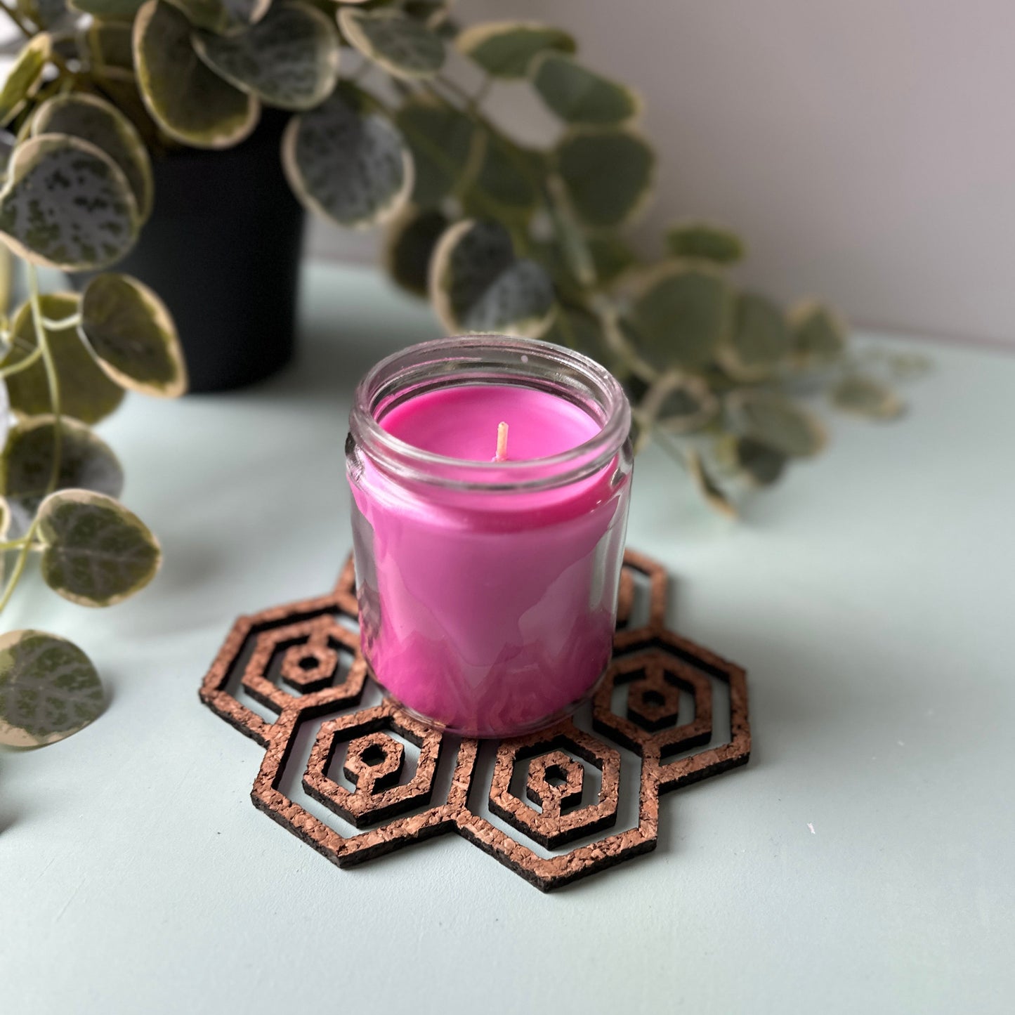 Pink candle in a glass jar on a honeycomb trivet on a light background