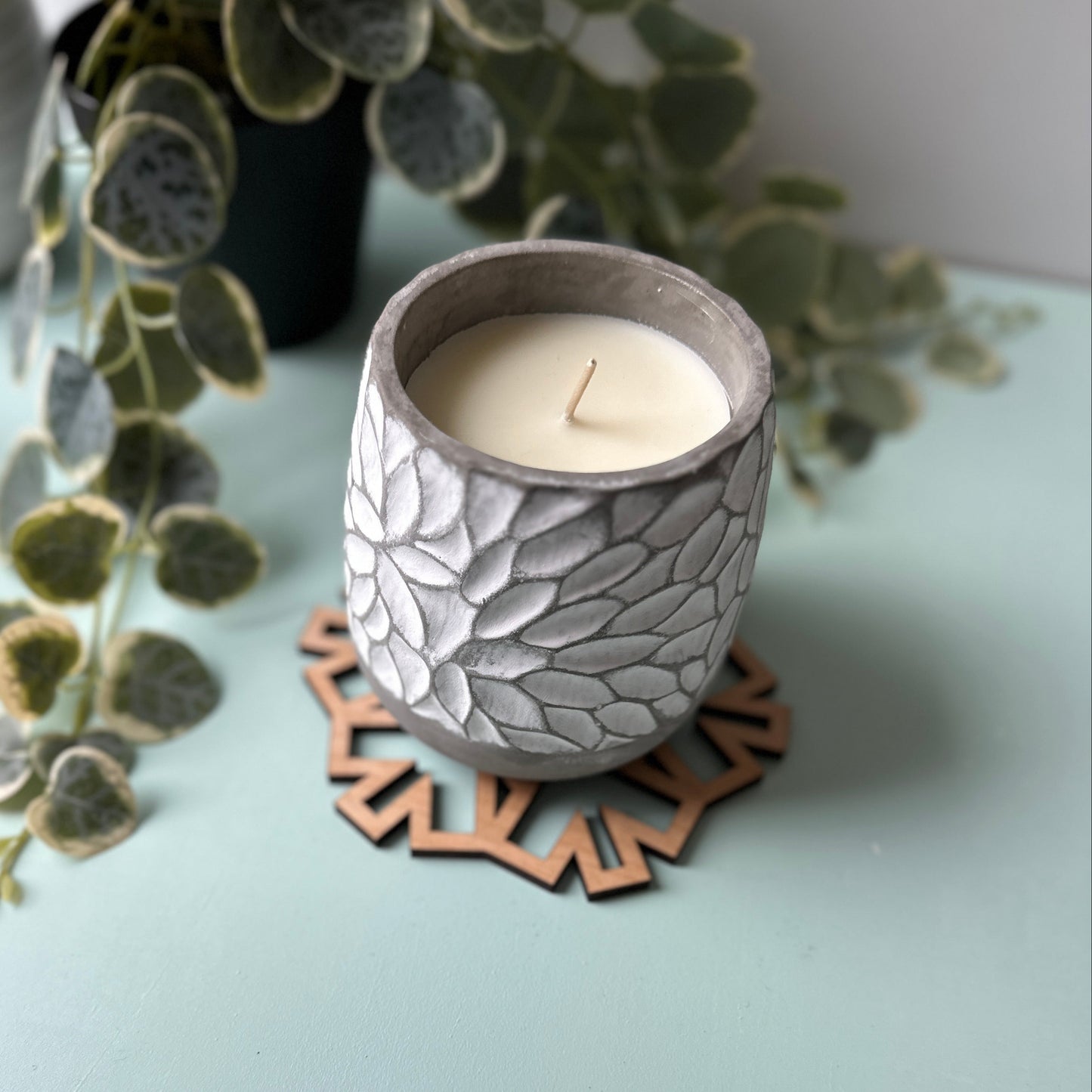 Decorative candle holder with a candle on a light surface, surrounded by greenery.