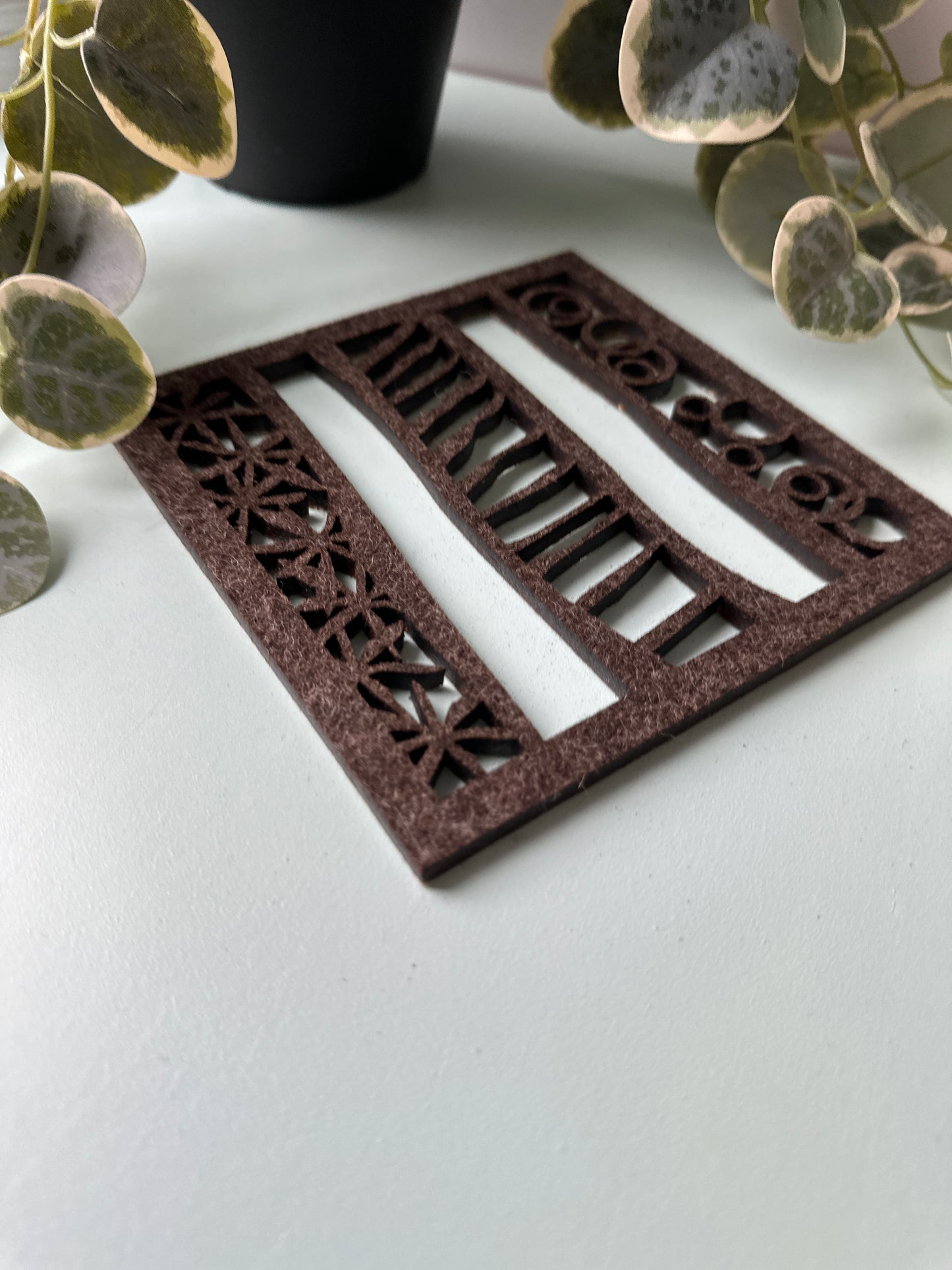 Decorative brown felt trivet with geometric pattern on a white background