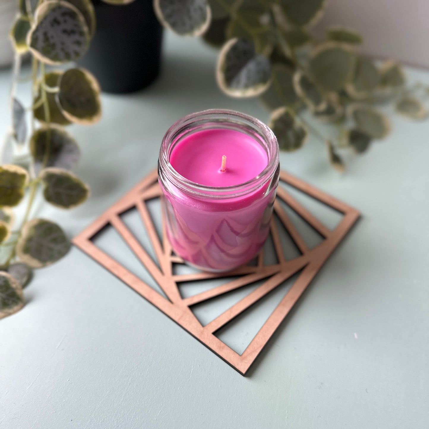 Pink candle in a glass holder on a laser-cut trivet with a decorative design