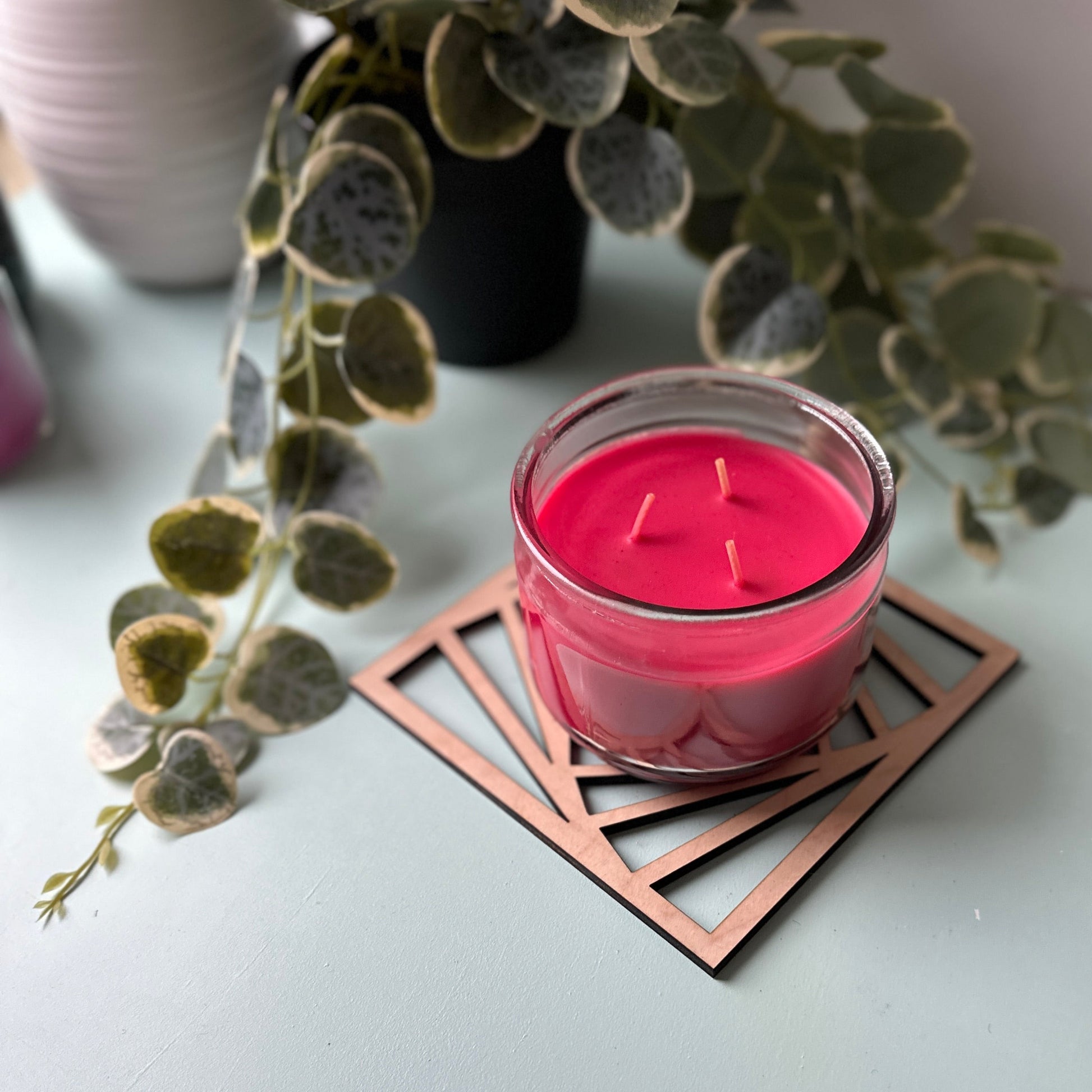Pink candle in a glass holder on a laser-cut trivet with a decorative design