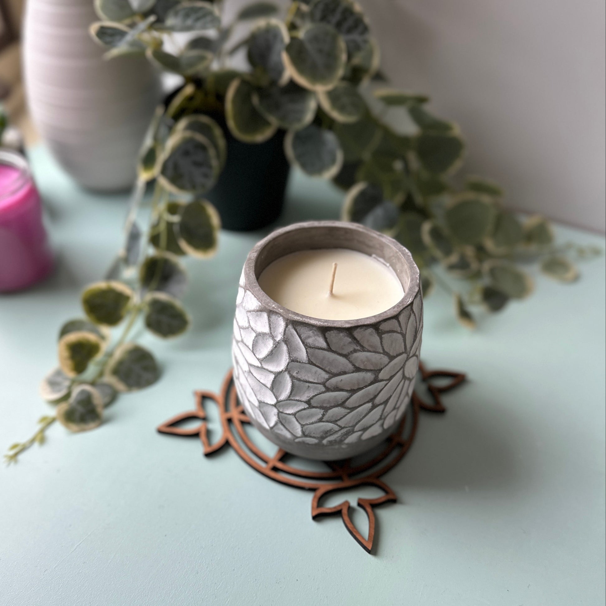 White candle in a decorative glass holder on a stained glass trivet with leaves in the background