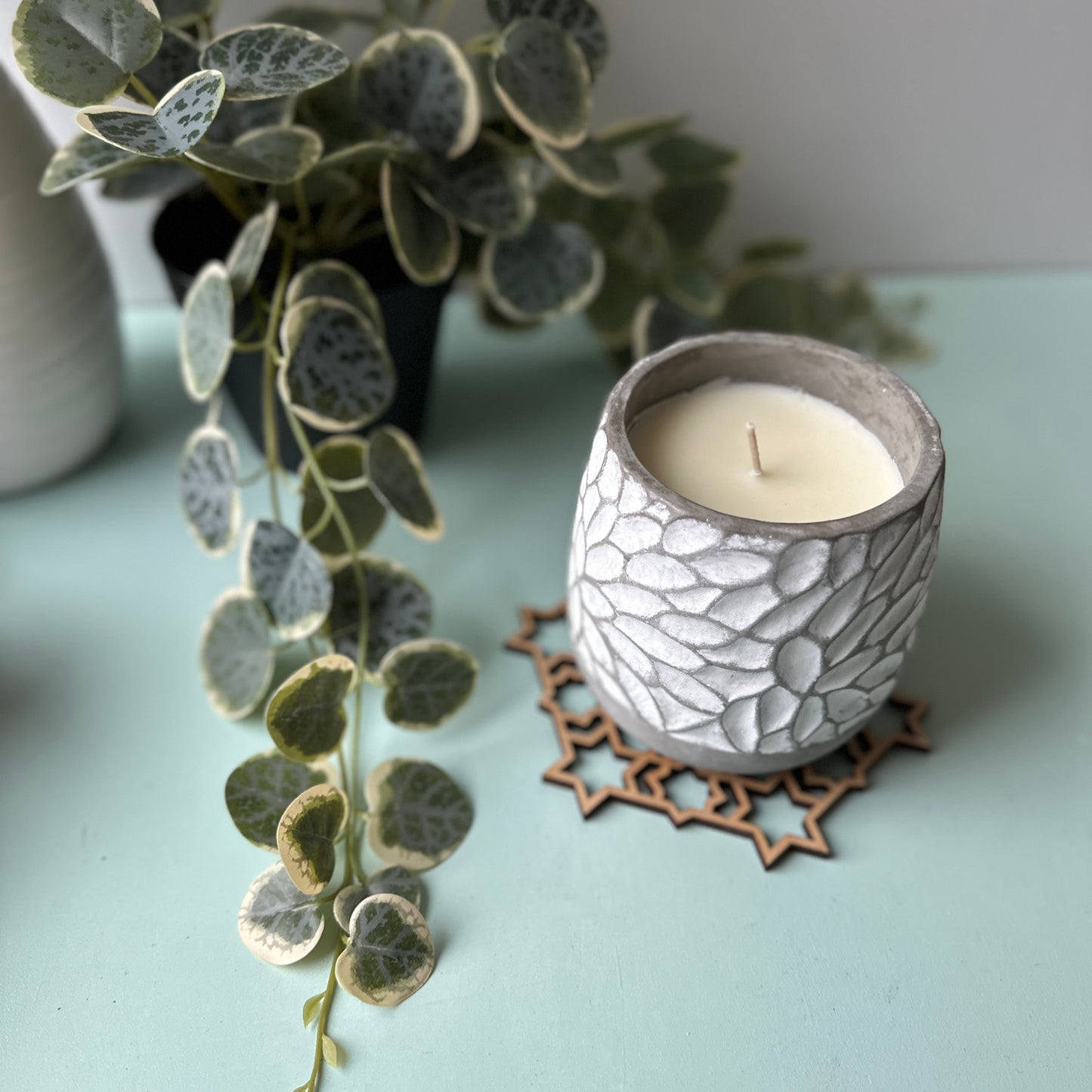 Ceramic candle holder with a candle on a trivet with a plant in the background