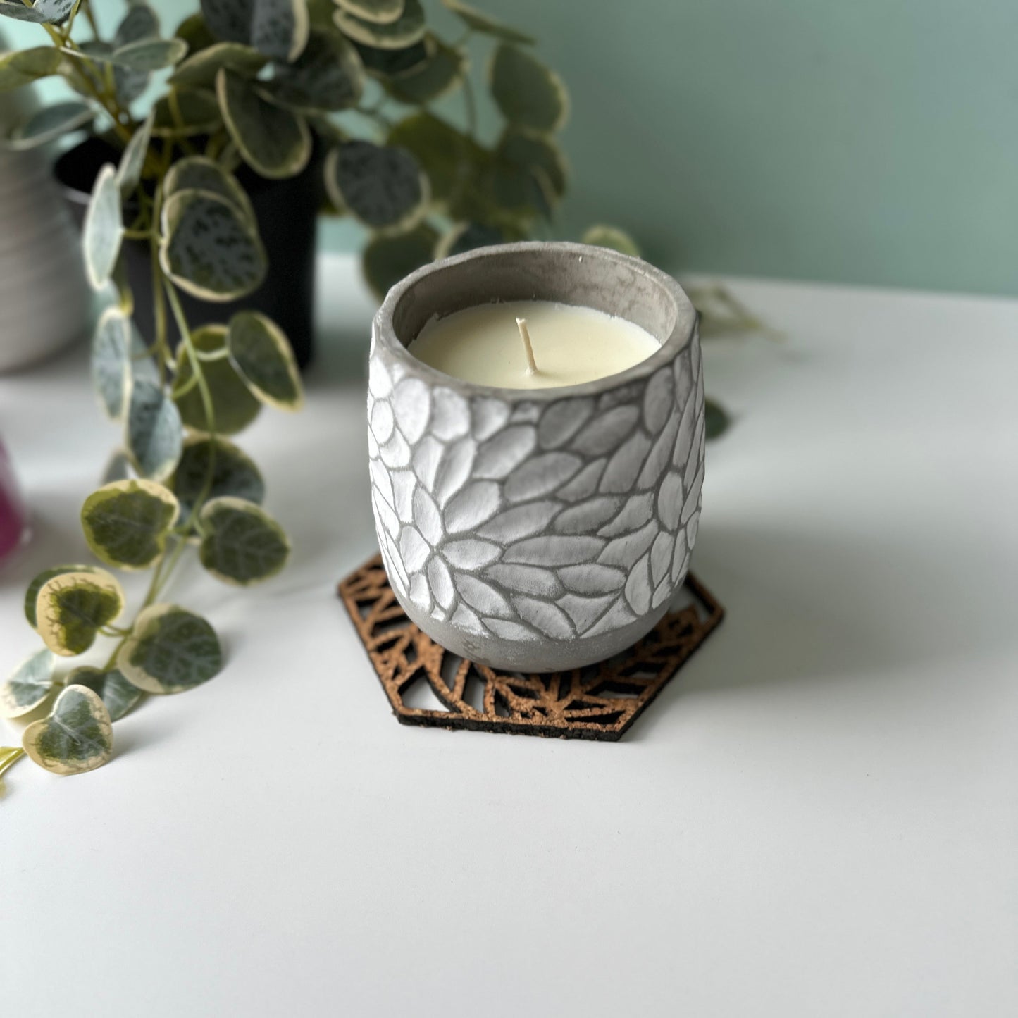 White candle on a decorative trivet with leaves and a photo frame in the background