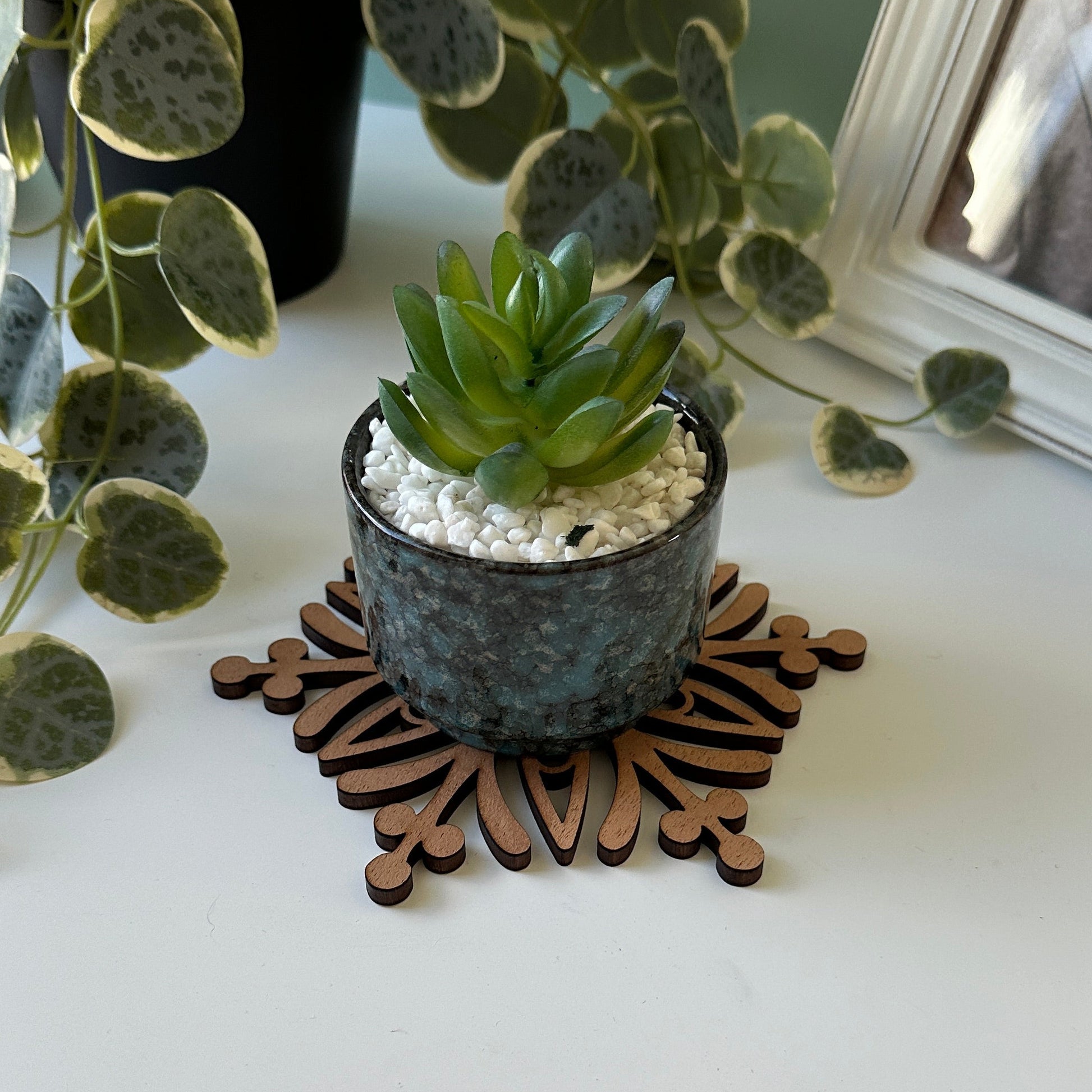 Decorative trivet with plants and a framed photo on a white wall.