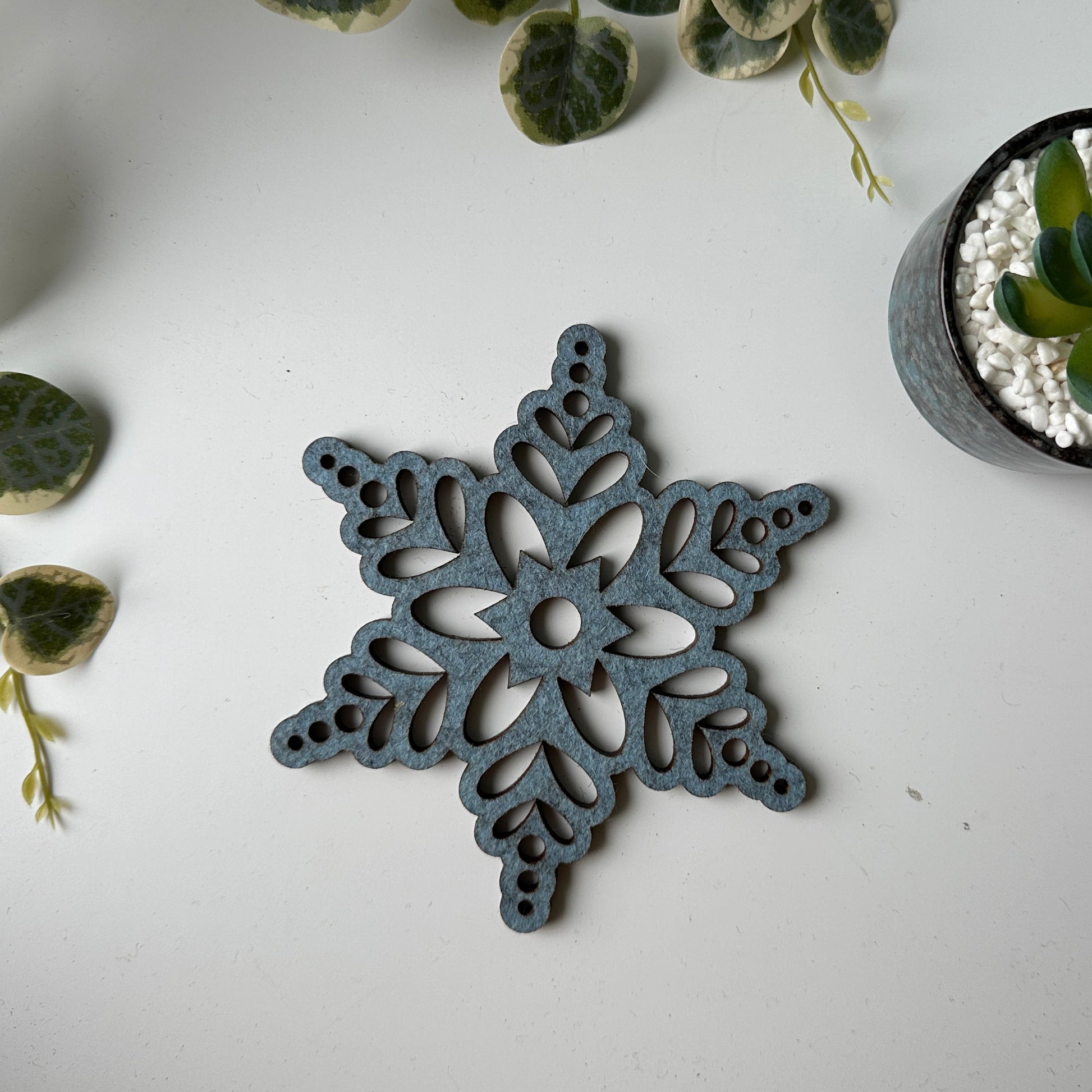 Decorative snowflake trivet on a white surface with plants
