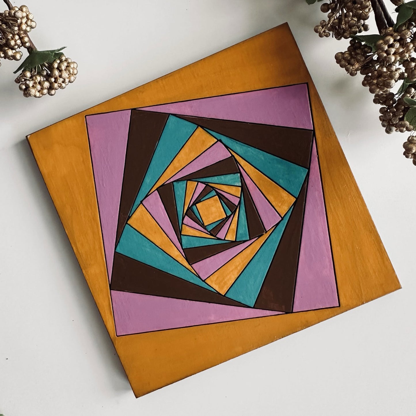 Colorful geometric spiral design on a wooden coaster with decorative elements.