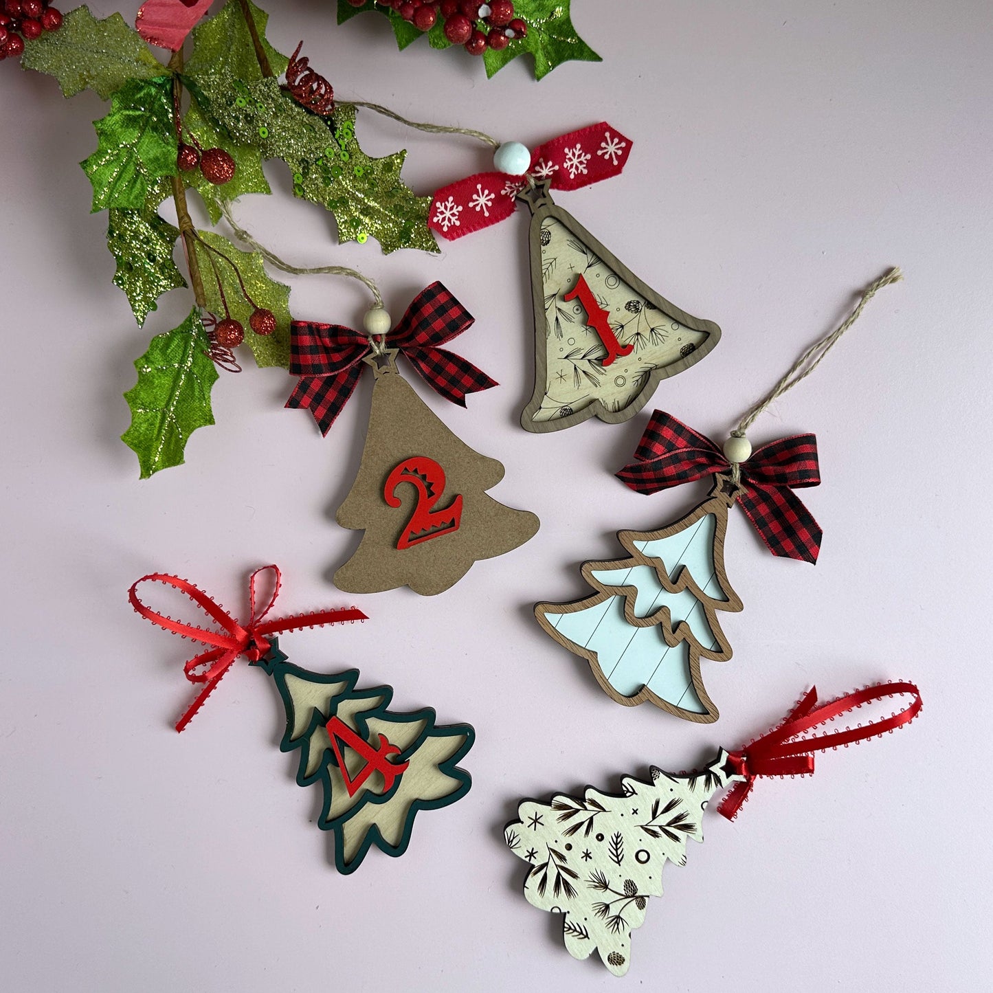 Laser-cut layered Christmas tree ornaments with red ribbon bows, hanging against a holiday backdrop