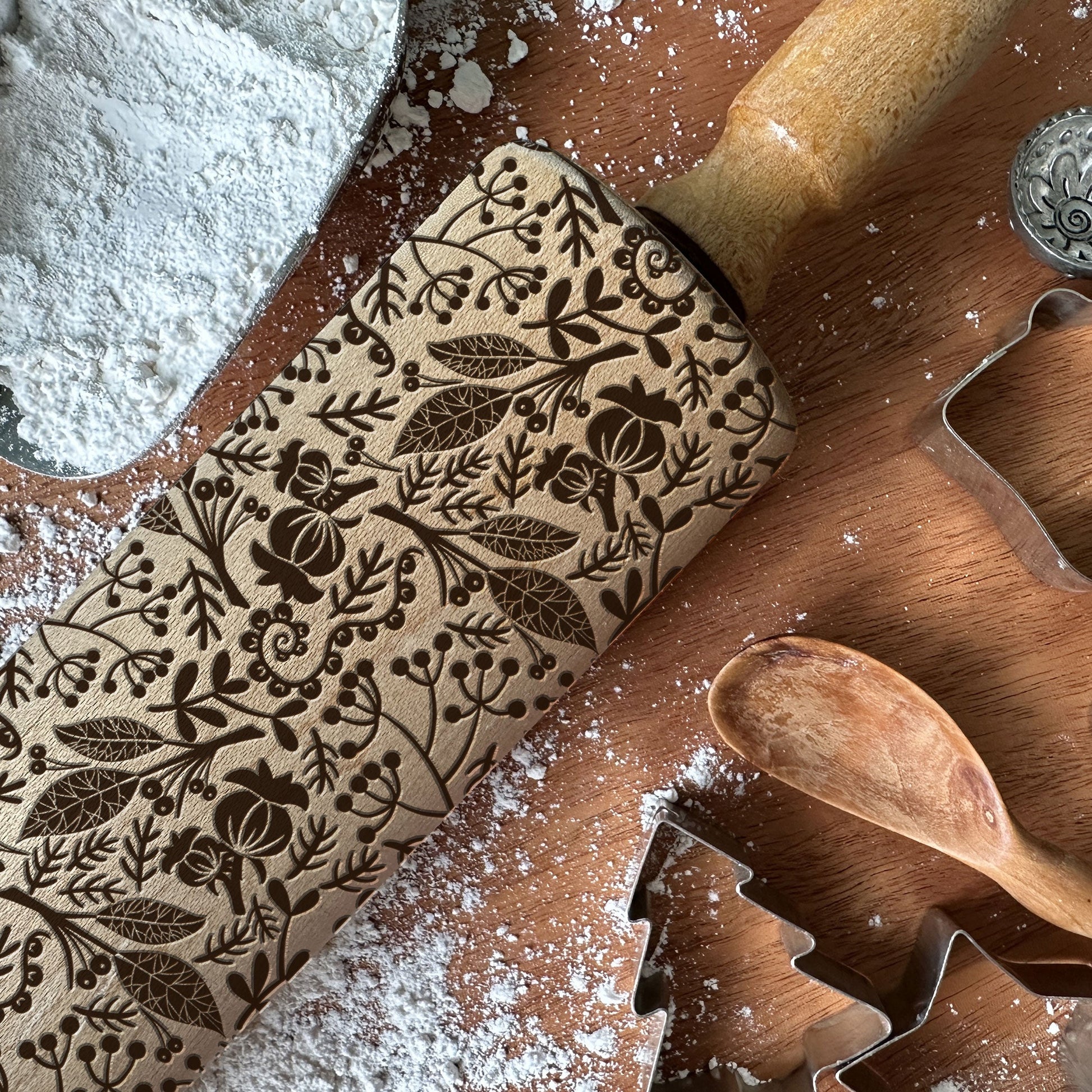 Decorative rolling pin with floral patterns on a wooden surface with cookie cutters and flour.