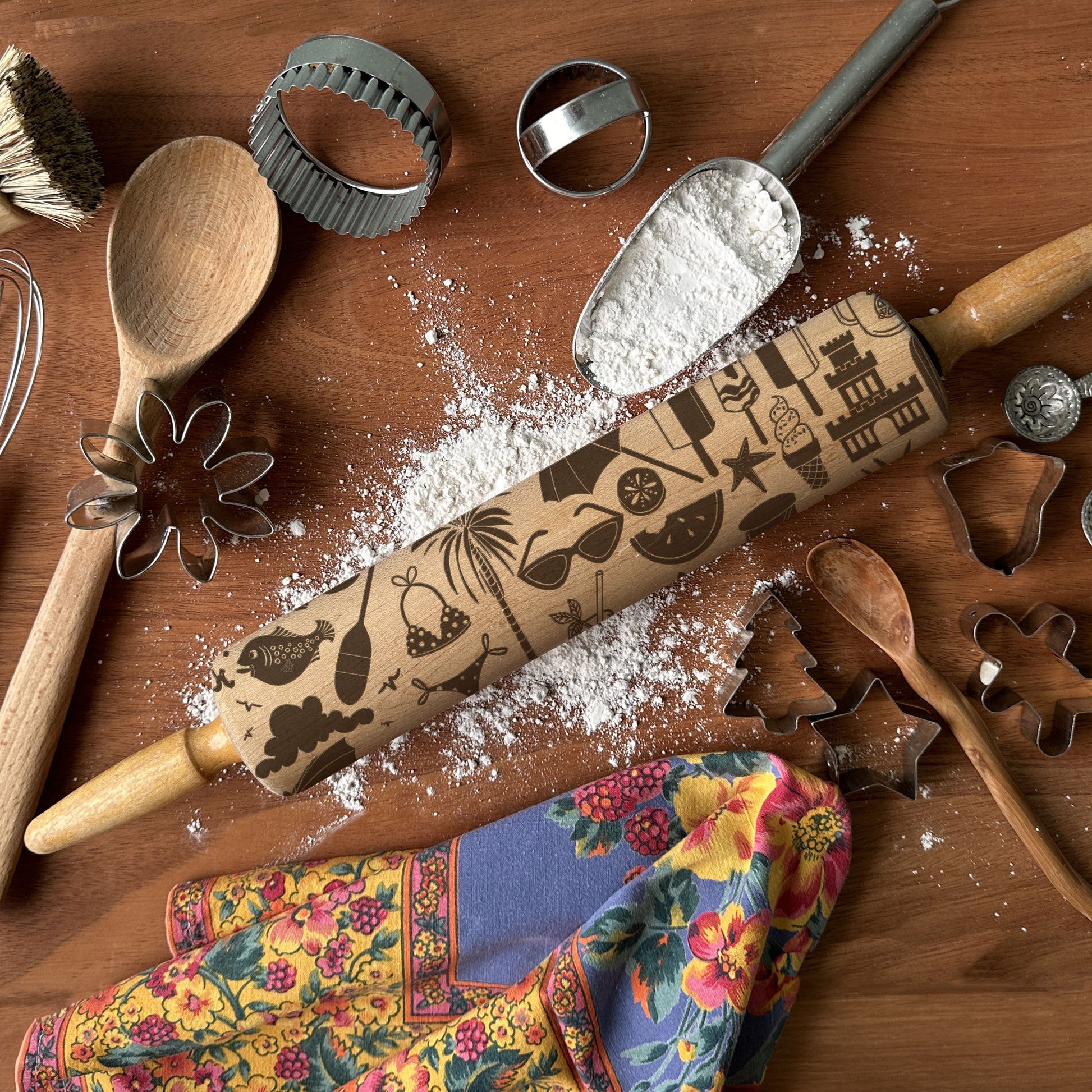 Wooden rolling pin with embossed designs on a wooden surface with flour and kitchen tools.