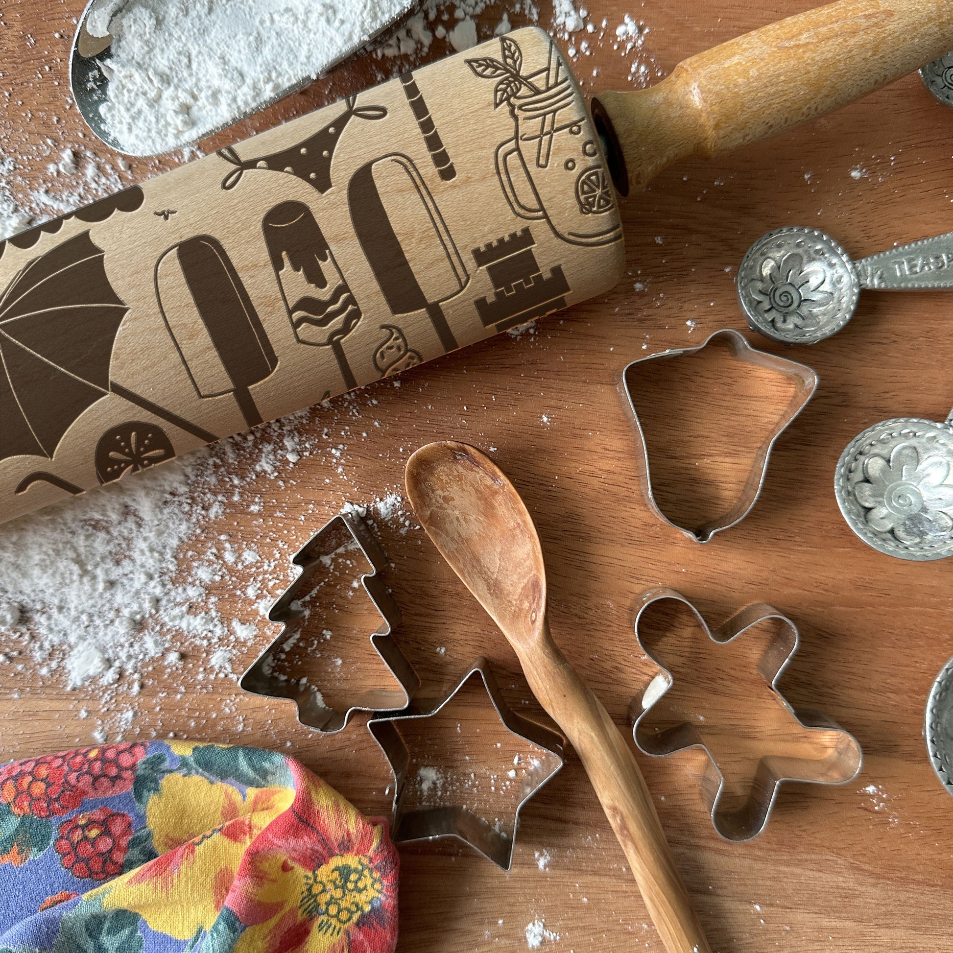 Wooden rolling pin with embossed designs and cookie cutters on a wooden surface with flour.