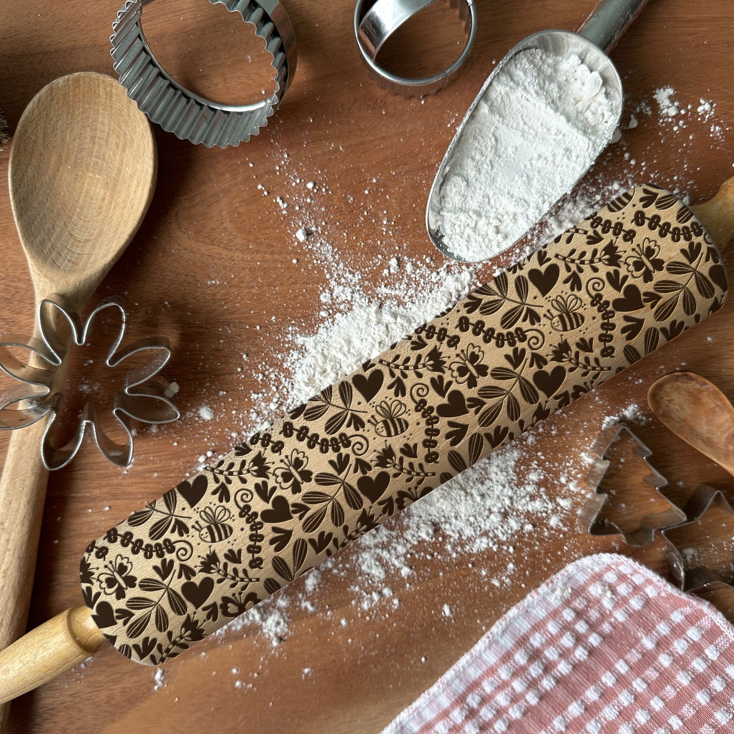 Decorative rolling pin with floral patterns on a wooden surface with flour and baking tools.