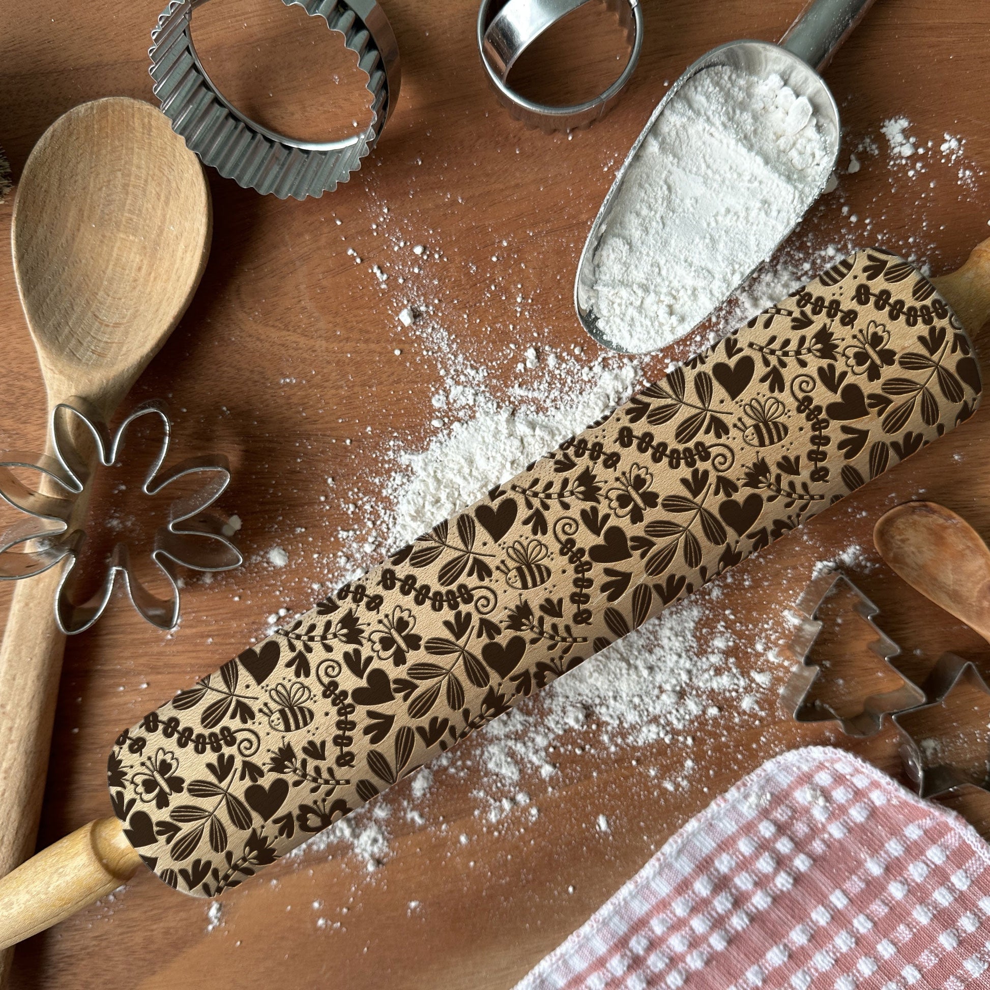 Decorative rolling pin with floral patterns on a wooden surface with flour and baking tools.