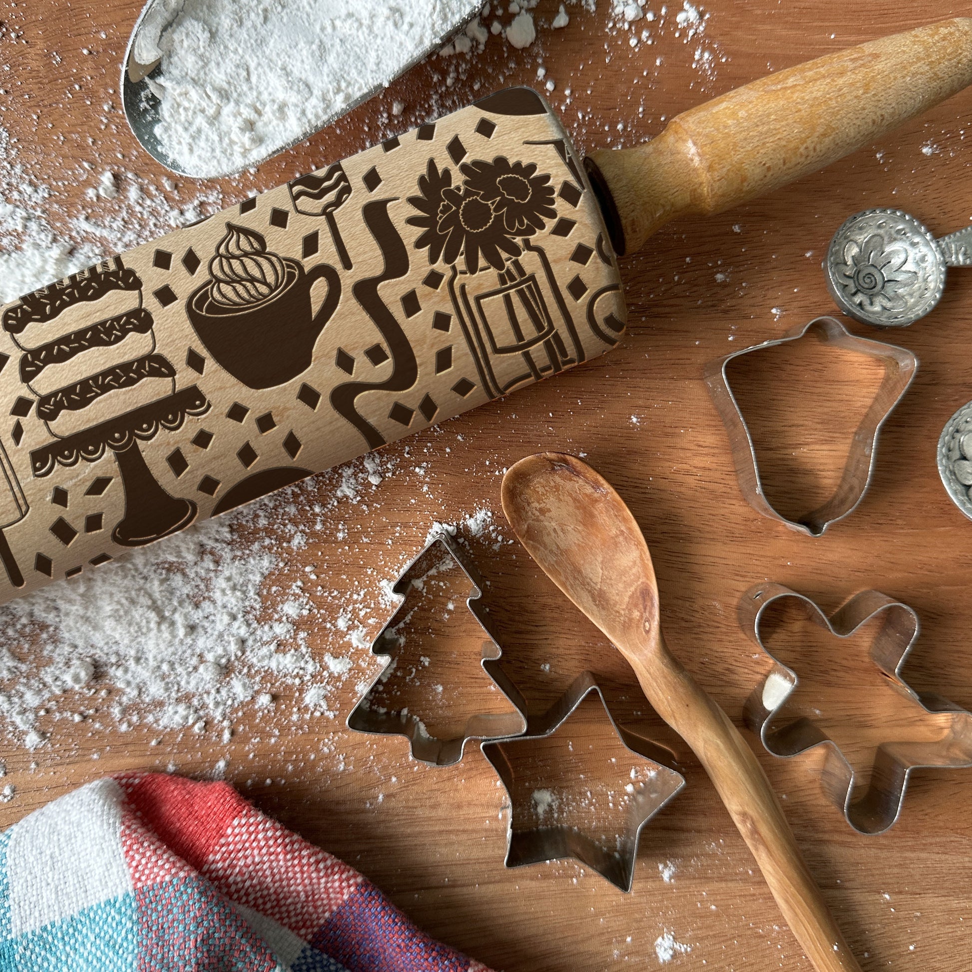 Baking tools including a rolling pin, cookie cutters, and an embossing rolling pin on a wooden surface with flour.