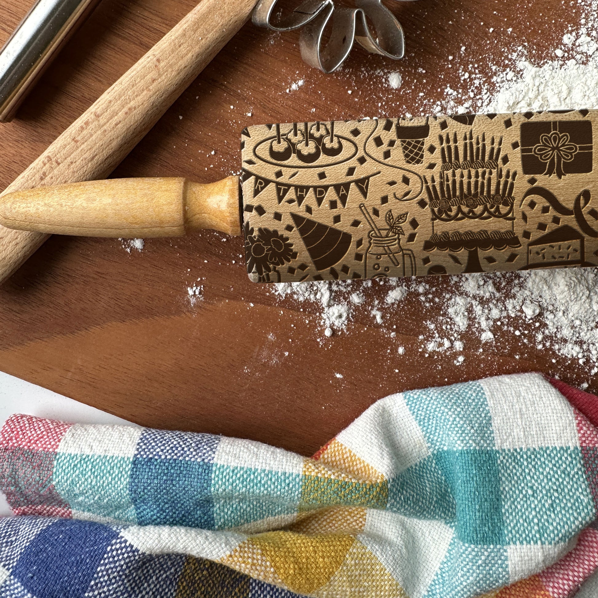 Wooden rolling pin with dinosaur pattern on a wooden surface with flour and checkered cloth.