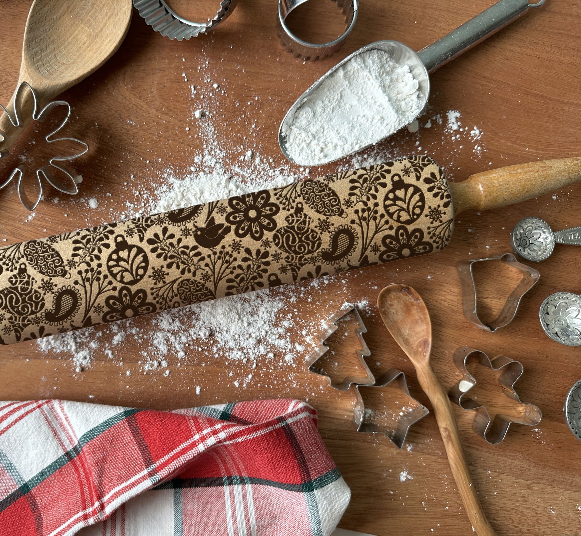 Decorative rolling pin with floral patterns on a wooden surface with flour and cookie cutters.