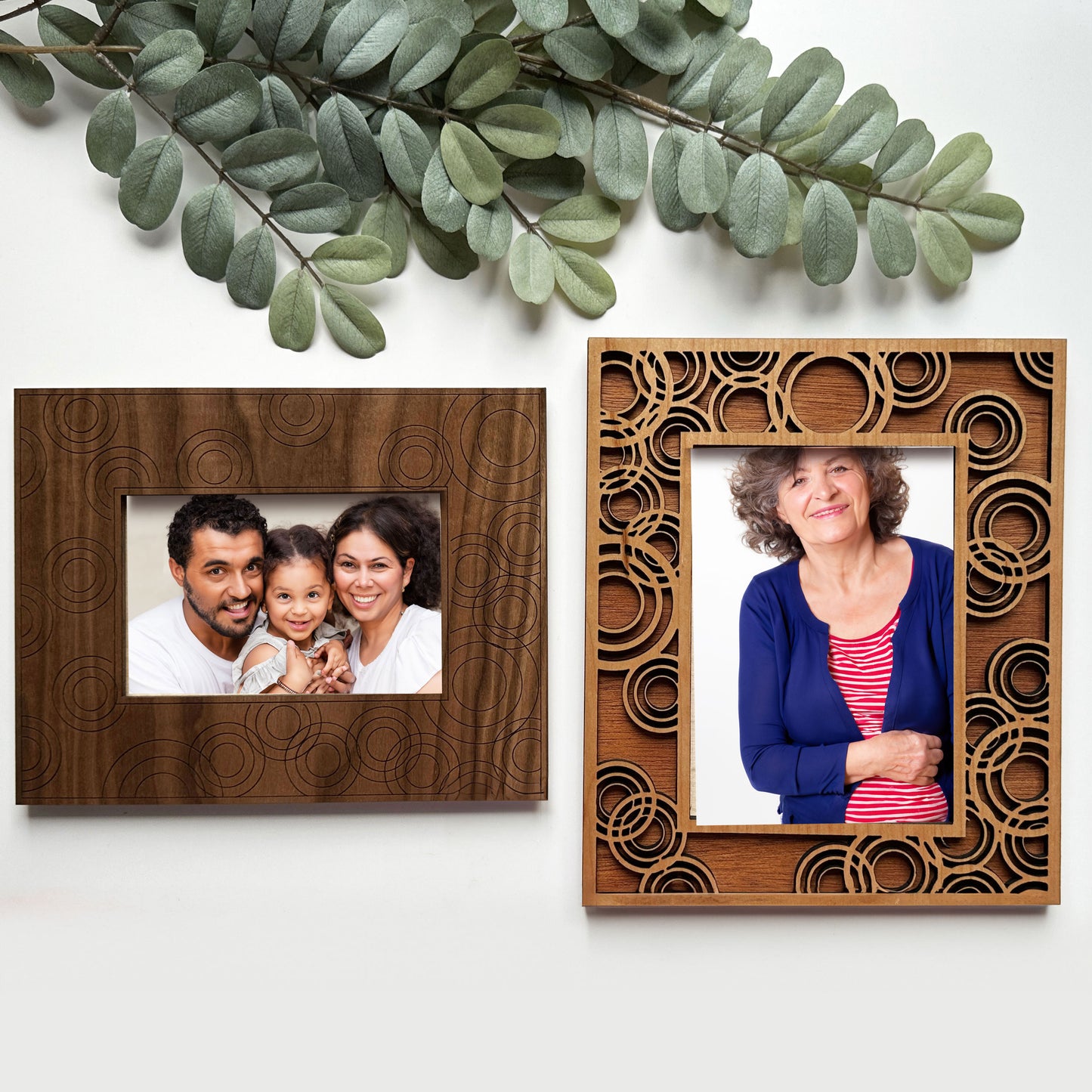 Two wooden photo frames with family portraits on a white background with green leaves.