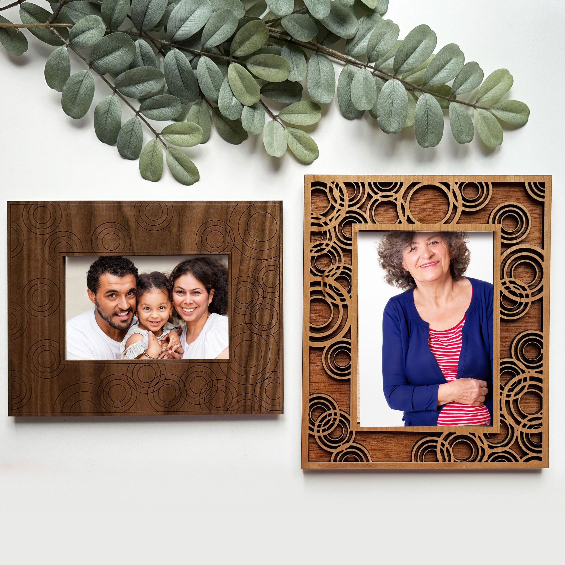 Two wooden photo frames with family portraits on a white background with green leaves.