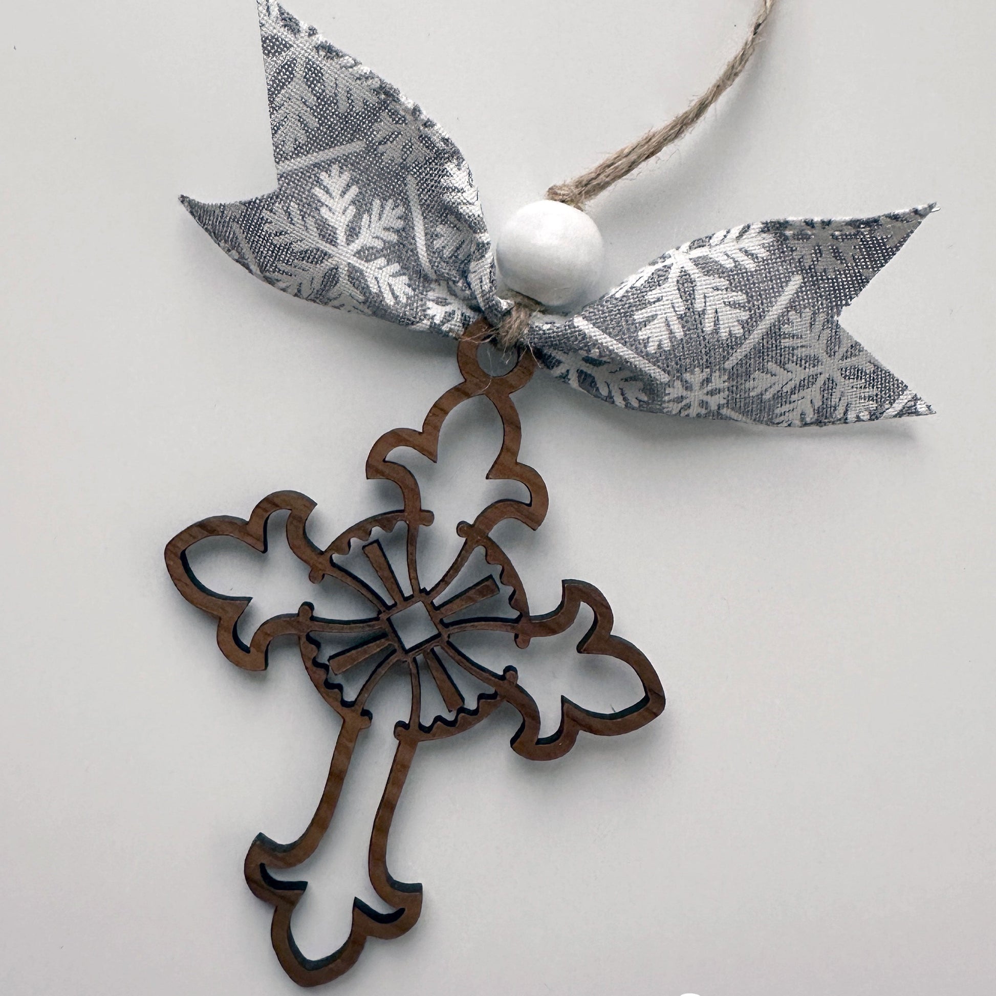 Decorative cross ornament with a gray ribbon featuring white snowflake patterns on a light gray background.