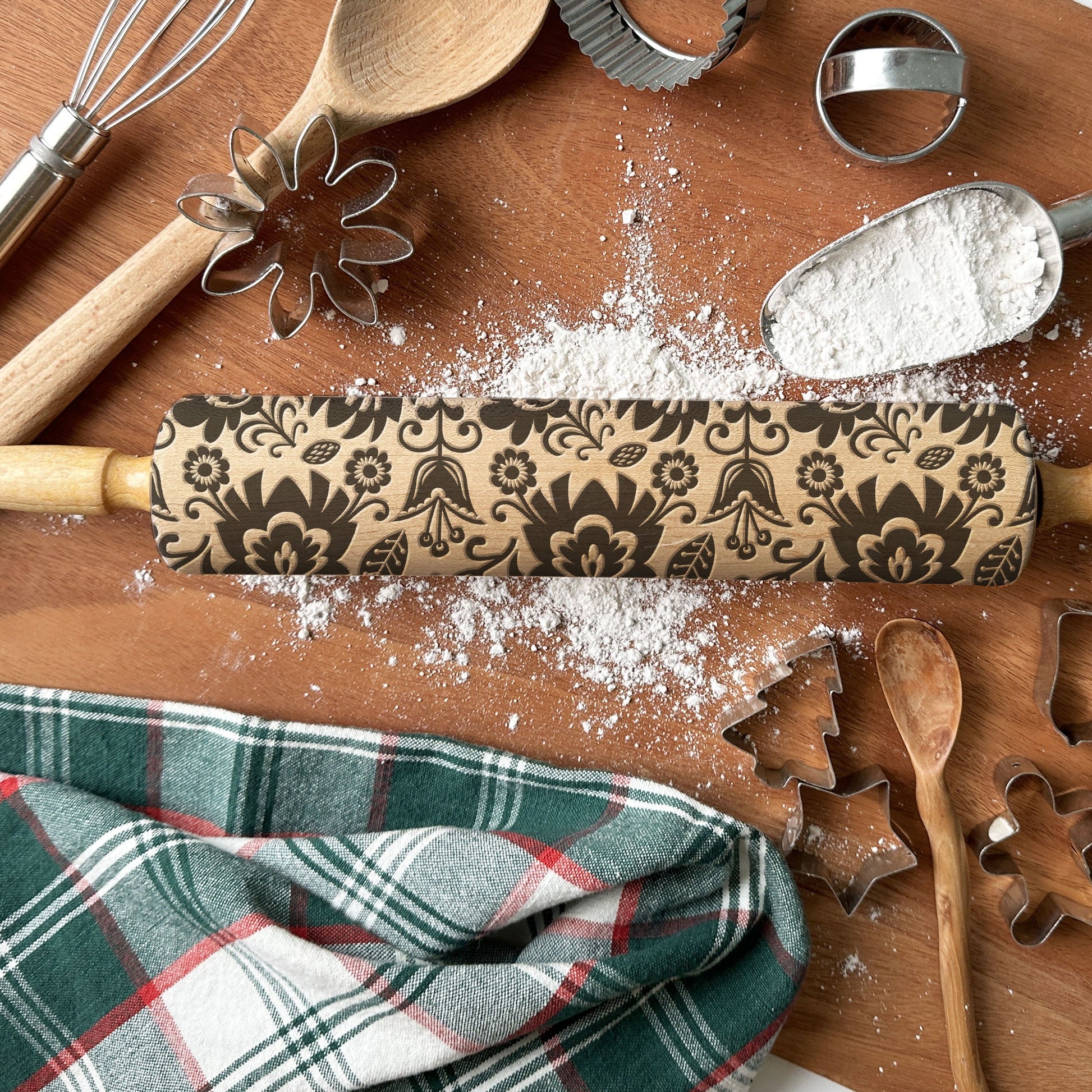 Decorative rolling pin with floral patterns on a wooden surface with baking tools.