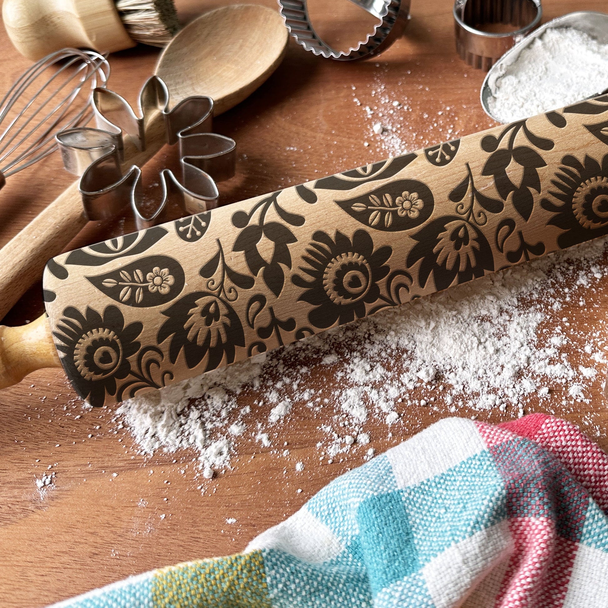 Decorative rolling pin with floral patterns on a wooden surface with baking tools.