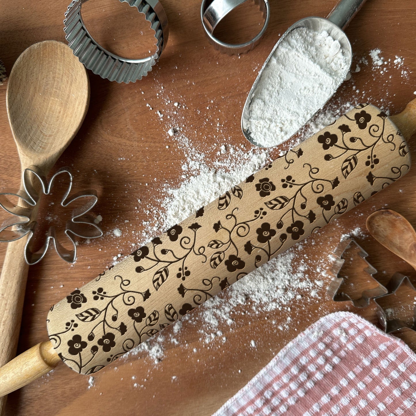 Decorative rolling pin with floral patterns on a wooden surface with flour and baking tools.