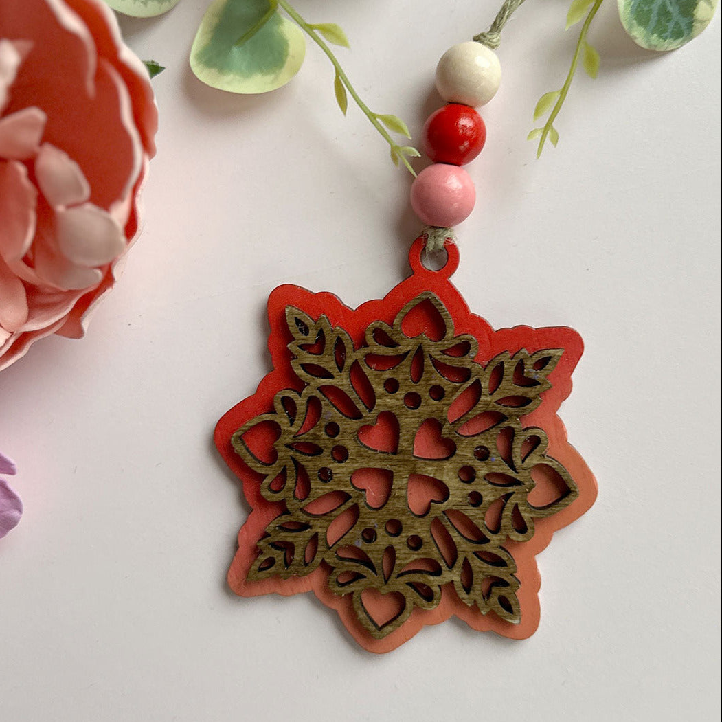 Decorative red and gold pendant with beads on a light background with flowers and leaves.