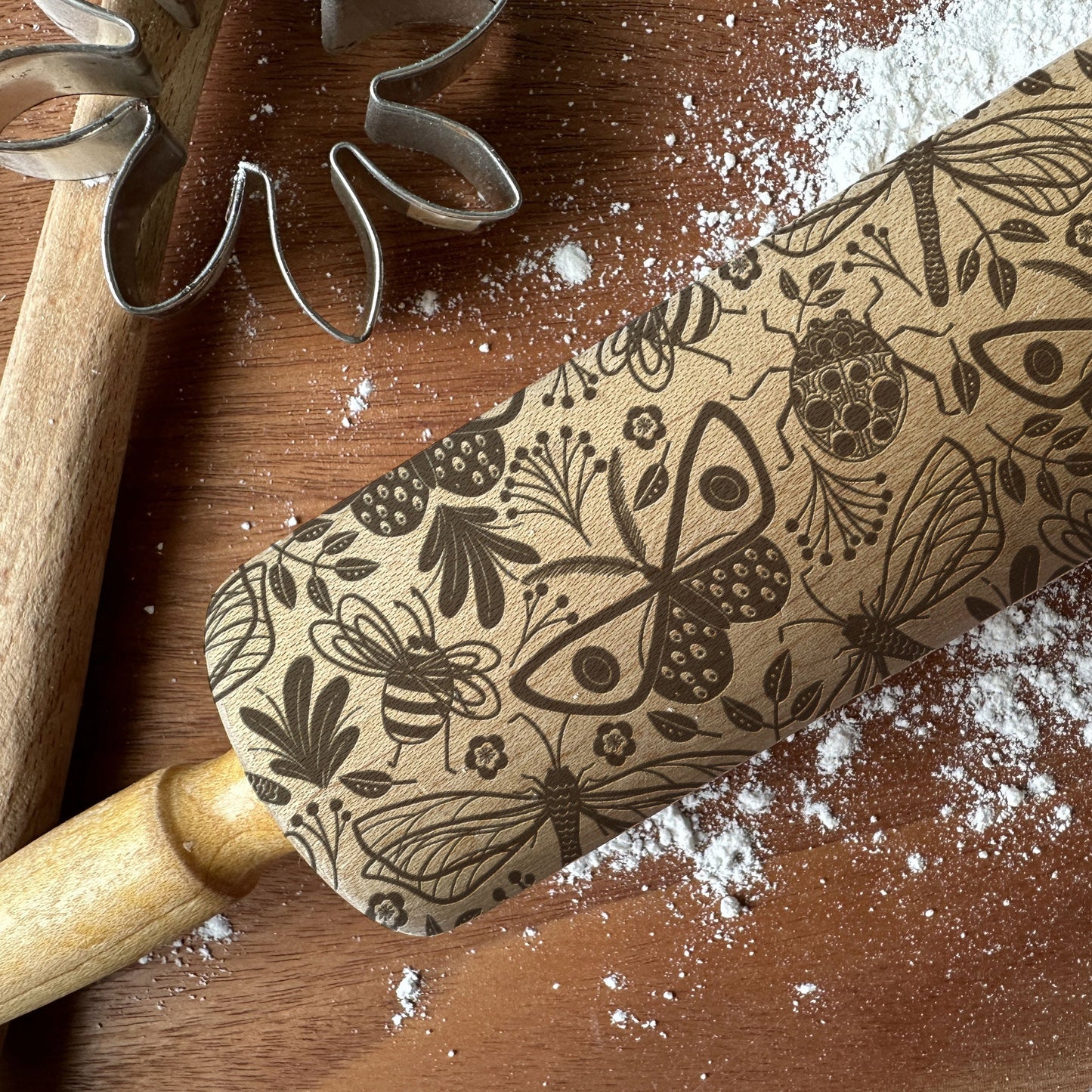 Wooden rolling pin with floral and butterfly patterns on a wooden surface with flour.