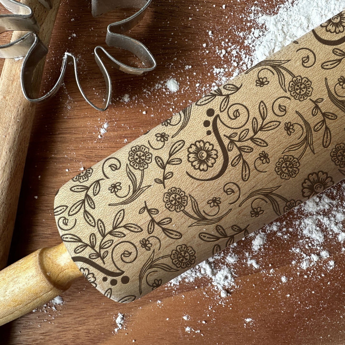 Decorative rolling pin with floral patterns on a wooden surface with flour.