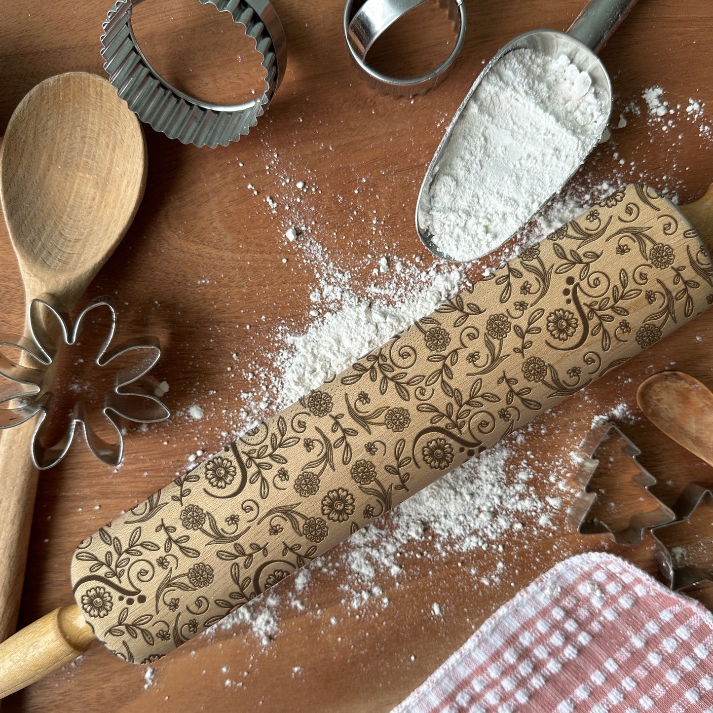 Decorative rolling pin with floral patterns on a wooden surface with flour and baking tools.