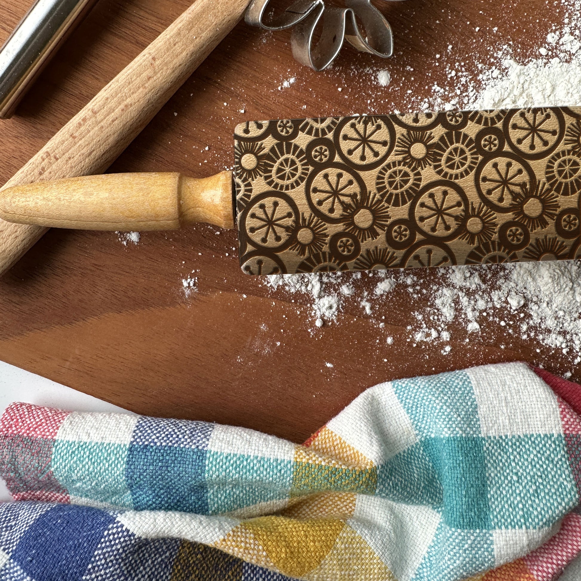 Decorative rolling pin with pattern on a wooden surface with flour and a checkered cloth.