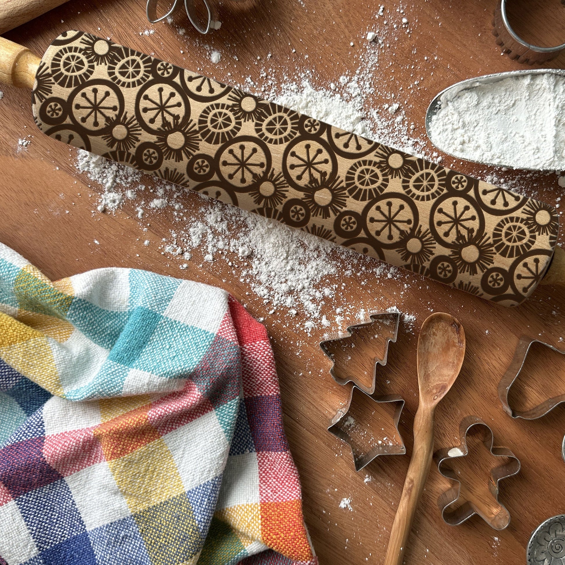 Decorative rolling pin with pattern on a wooden surface with baking tools and flour.