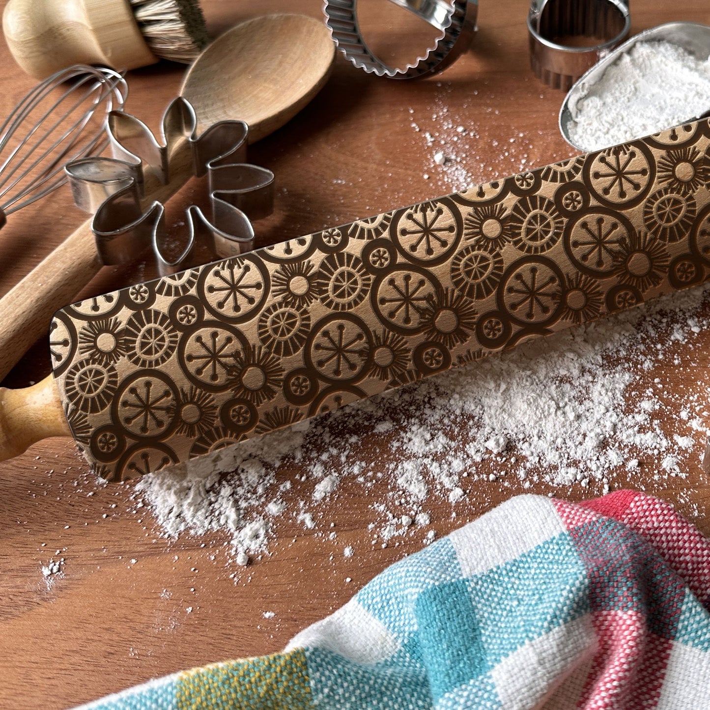 Decorative rolling pin with embossed patterns on a wooden surface with flour and kitchen tools.