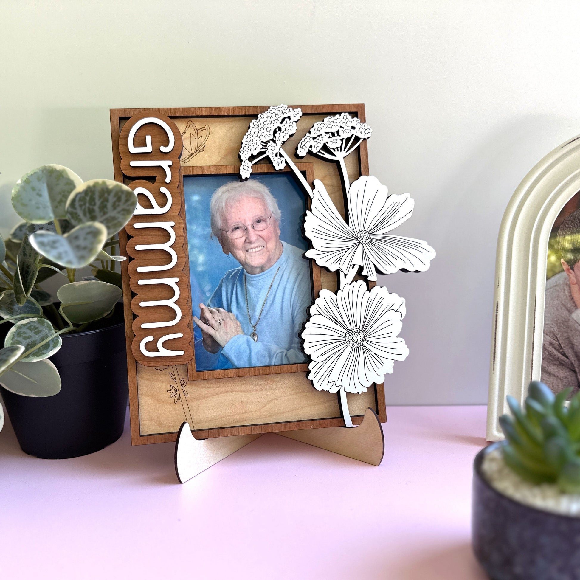 Wooden photo frame with floral design and 'Grammy' text, placed on a surface with plants.