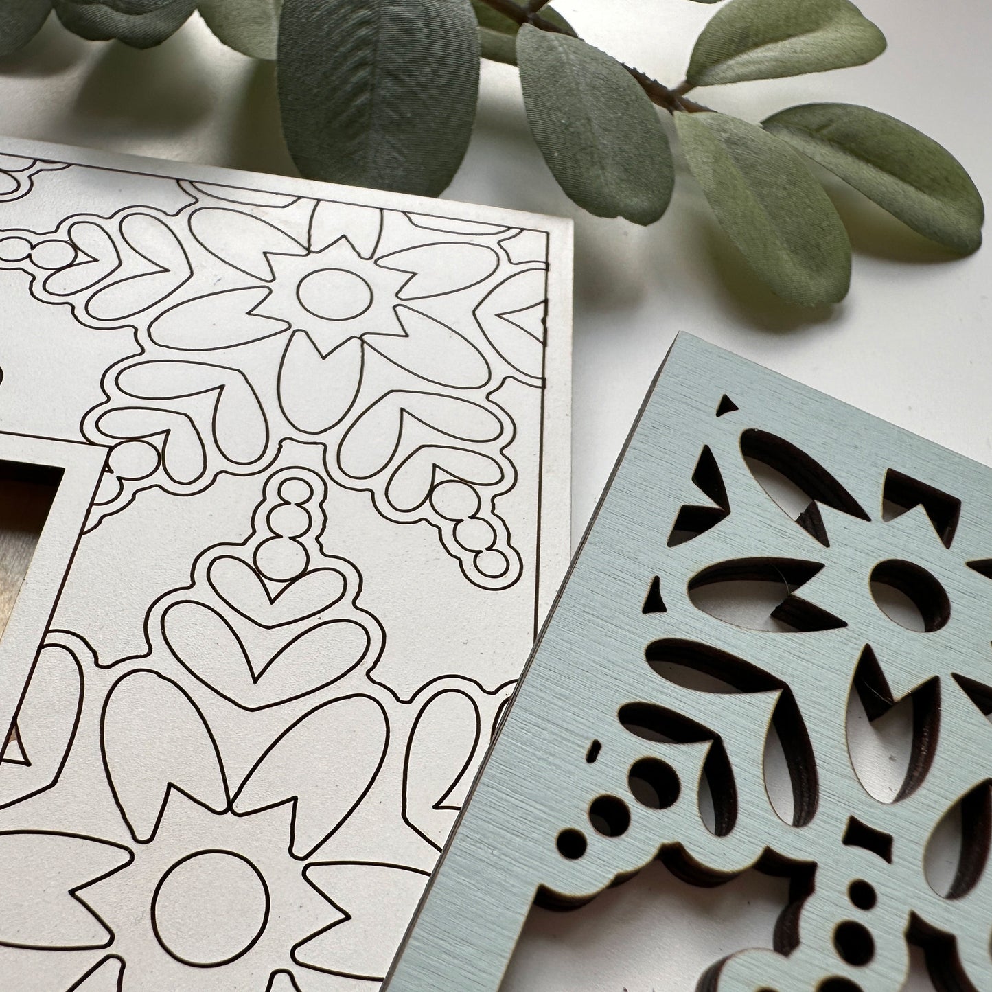 Decorative metal cutout with intricate patterns next to a coloring book page with similar designs.