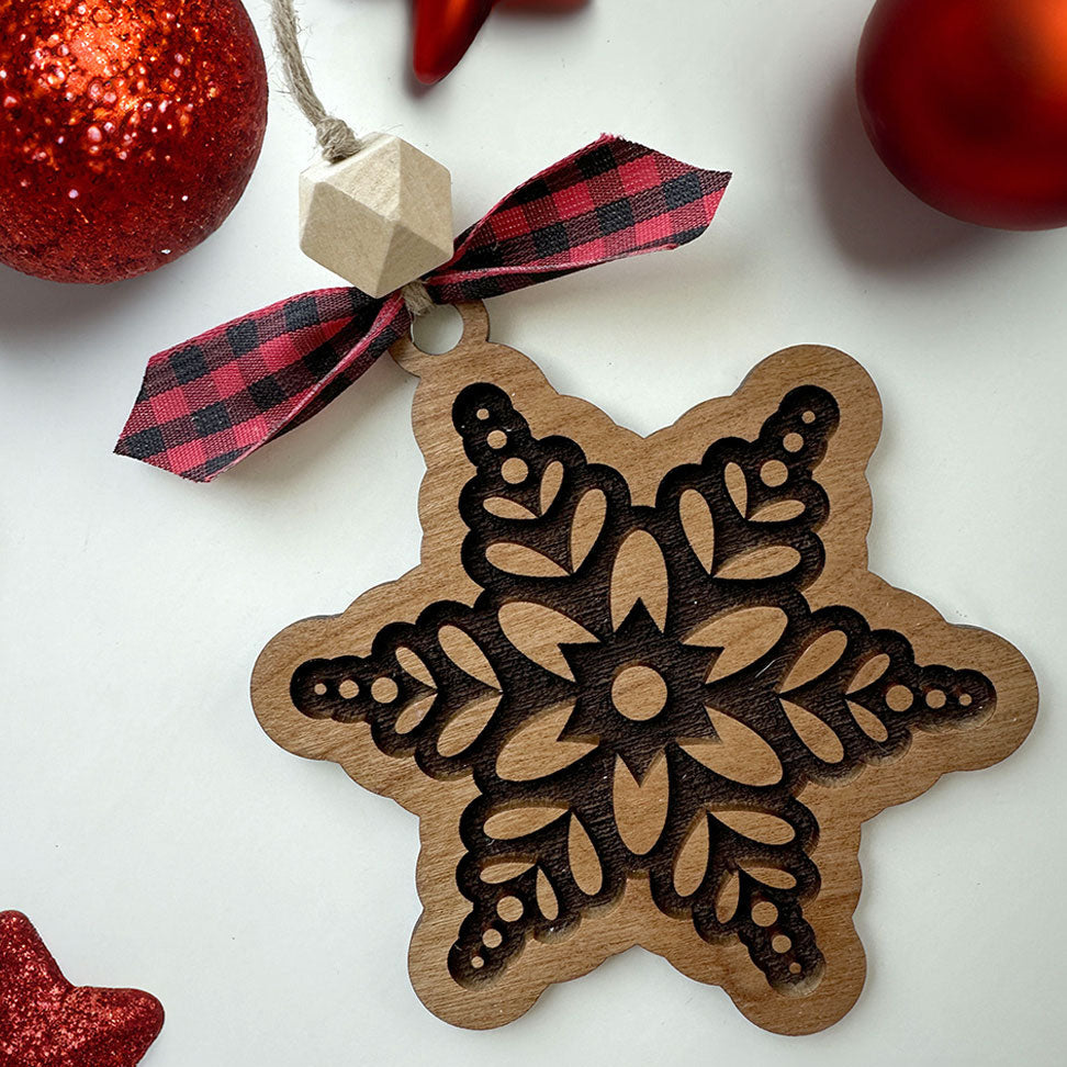 Wooden snowflake ornament with a red plaid ribbon on a white background with red Christmas balls and stars.